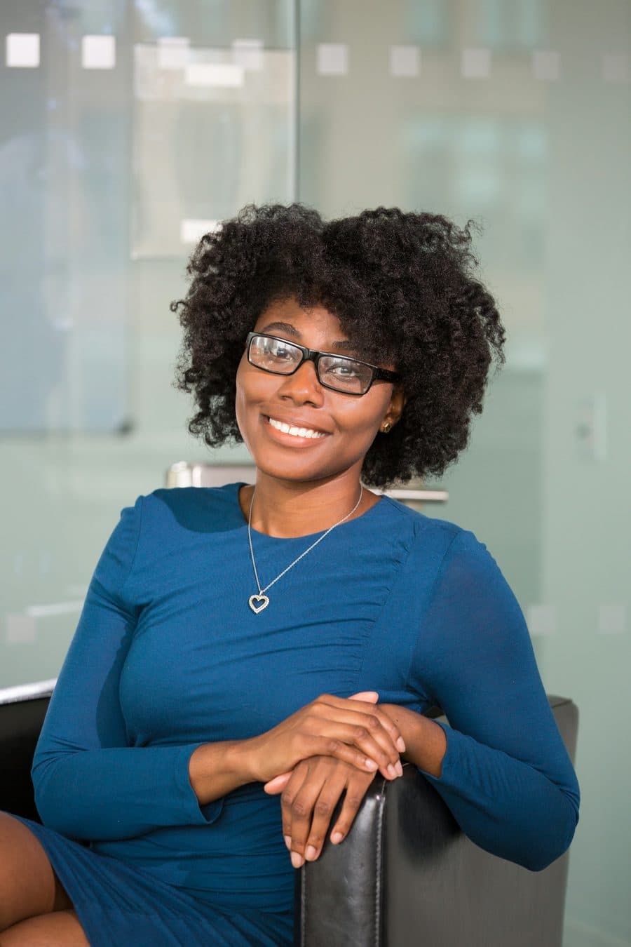Portrait of Amara Osei, a hygienist wearing glasses and a blue dress, seated and smiling