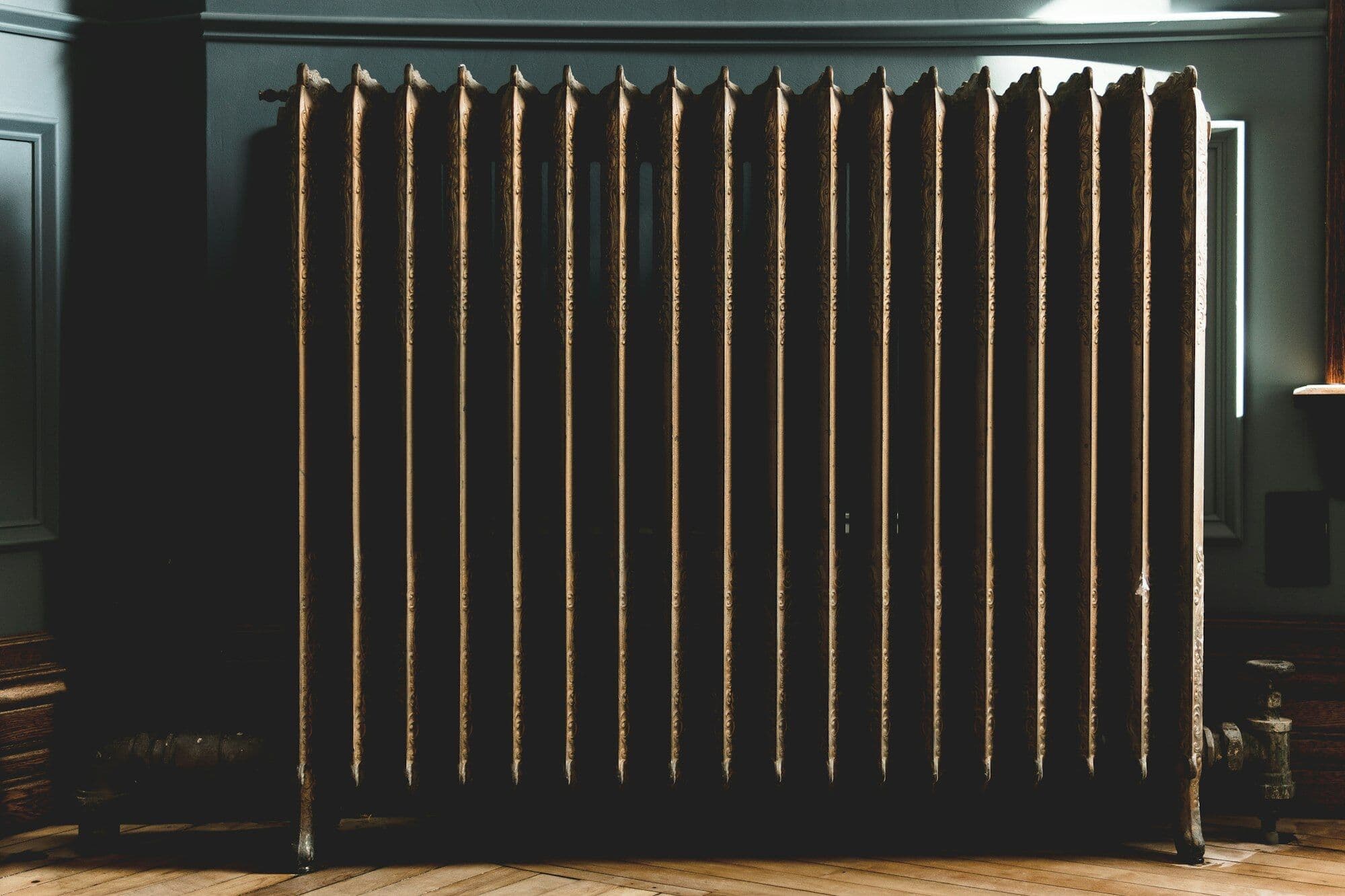 A dark cast-iron column radiator against a deep green wall