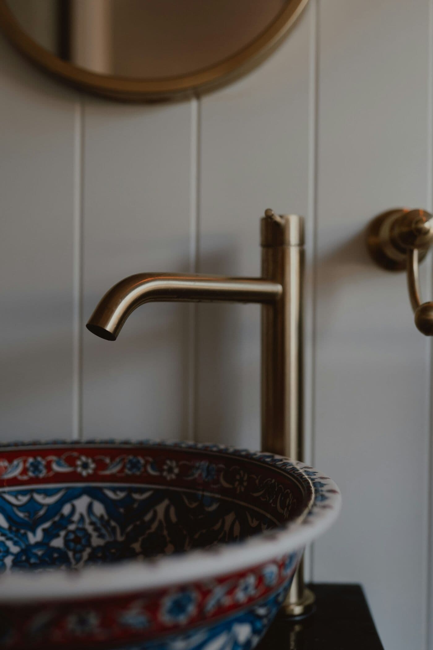 A brushed brass basin tap against pale tiles