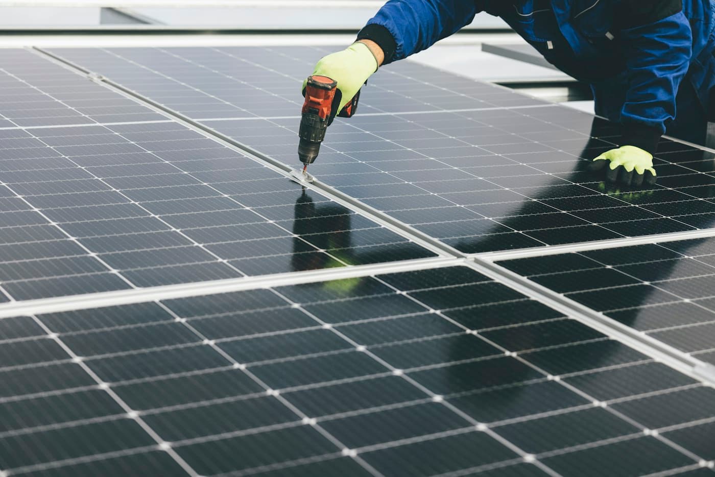 A gloved hand fixing a solar panel to its mounting rail with a drill