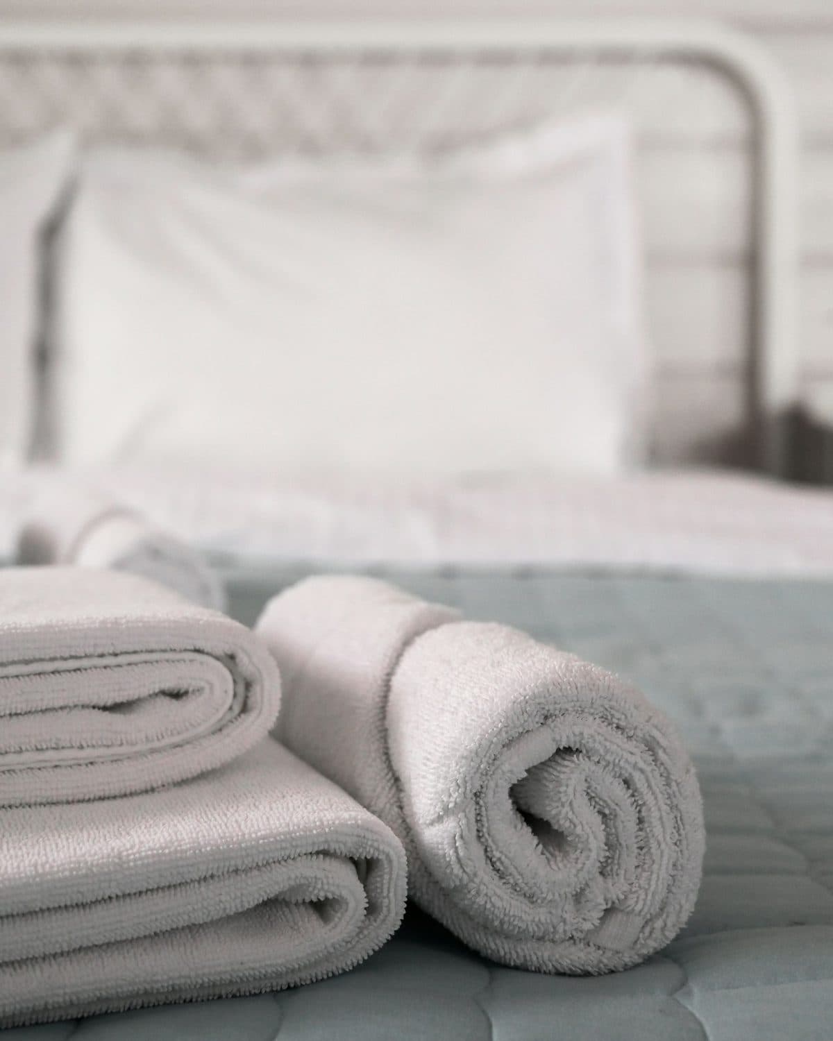 Freshly folded white towels stacked on a made bed
