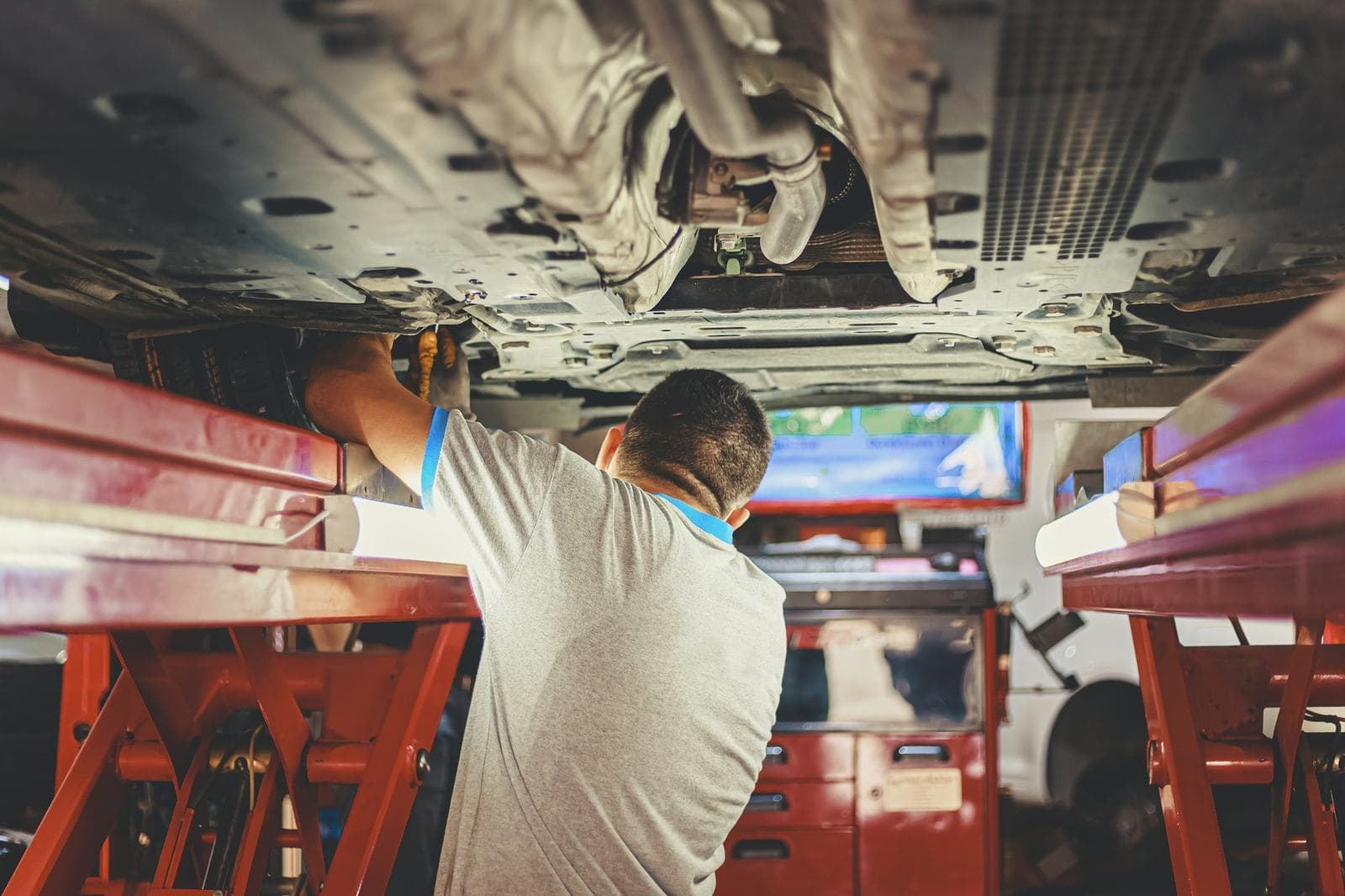 A technician working under a car raised on a red workshop lift