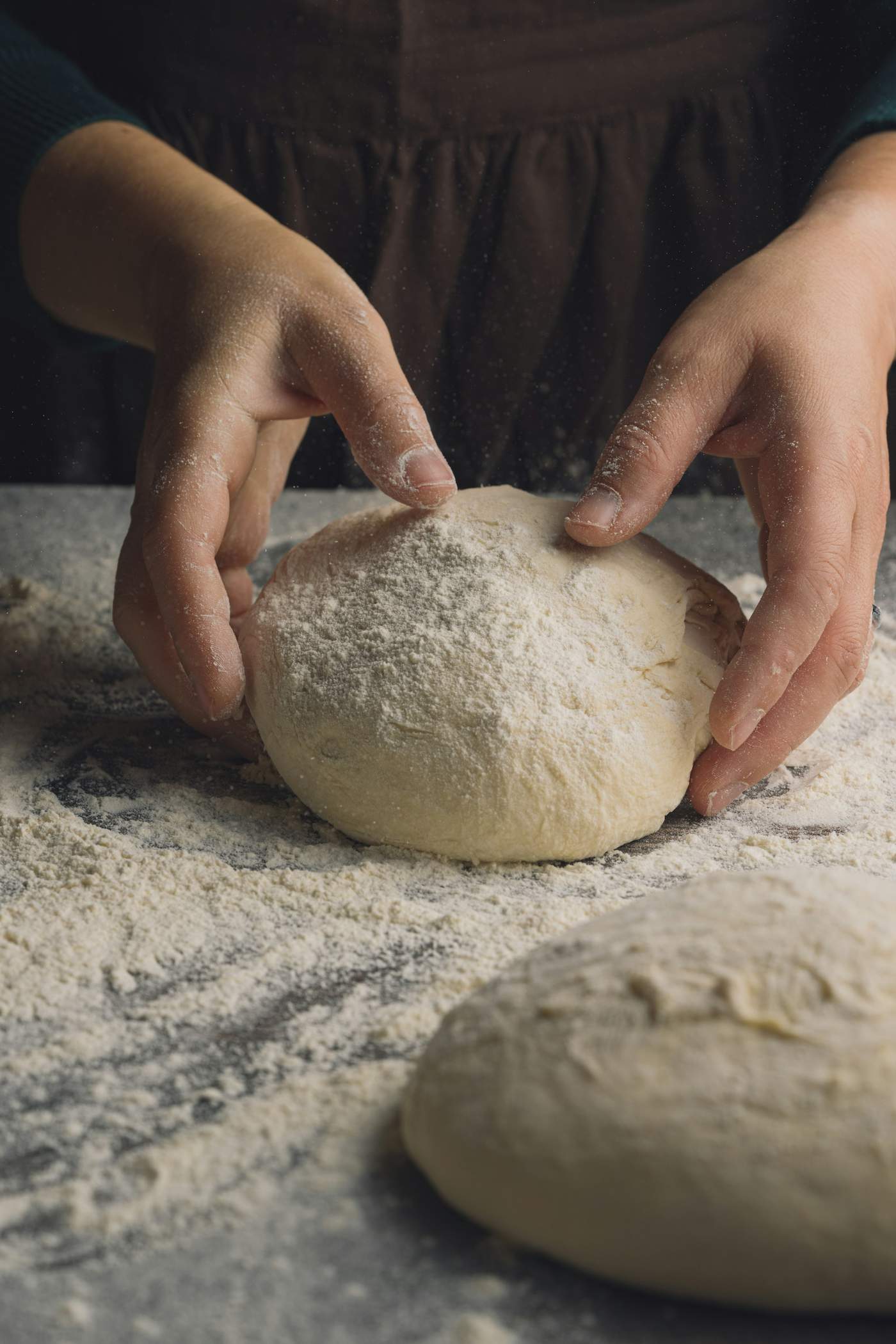 Floured hands shaping a ball of dough on a dusted worktop