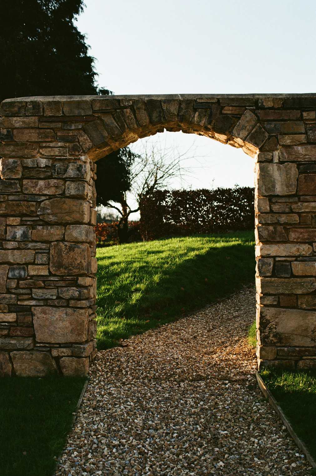 A stone archway opening onto a gravel path and lawn