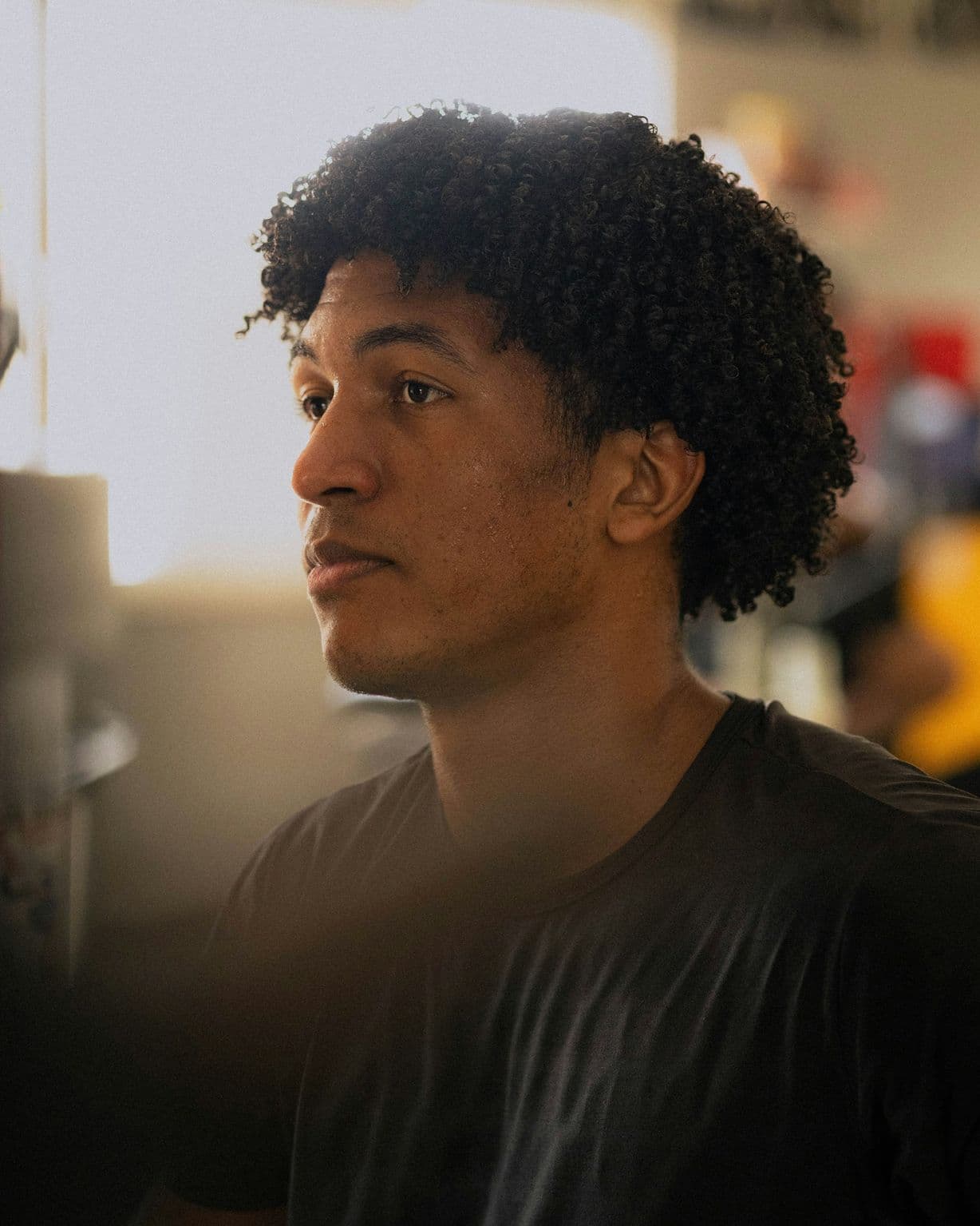 A young coach with curly hair in a dark T-shirt, looking across the gym