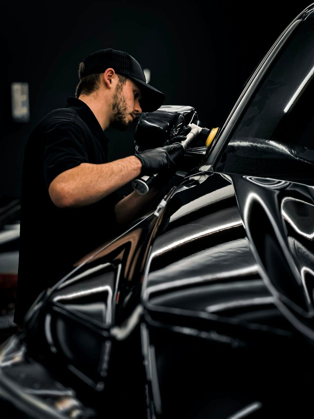 A detailer machine-polishing the bonnet of a dark car