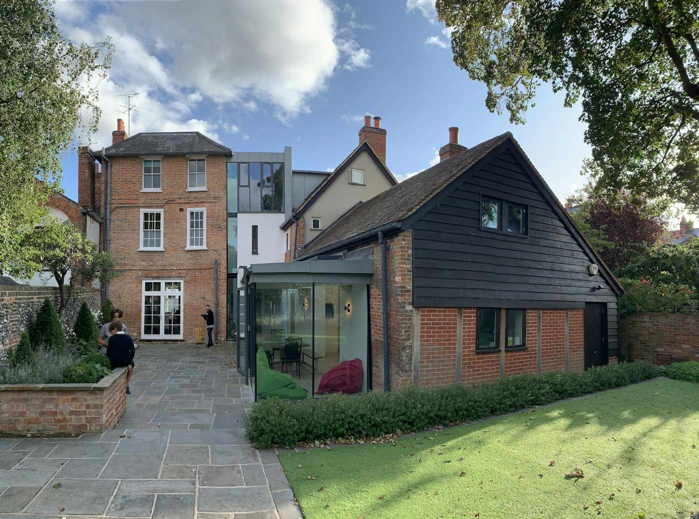 A red-brick rear extension with black timber cladding and a glazed link, beside a stone-paved path