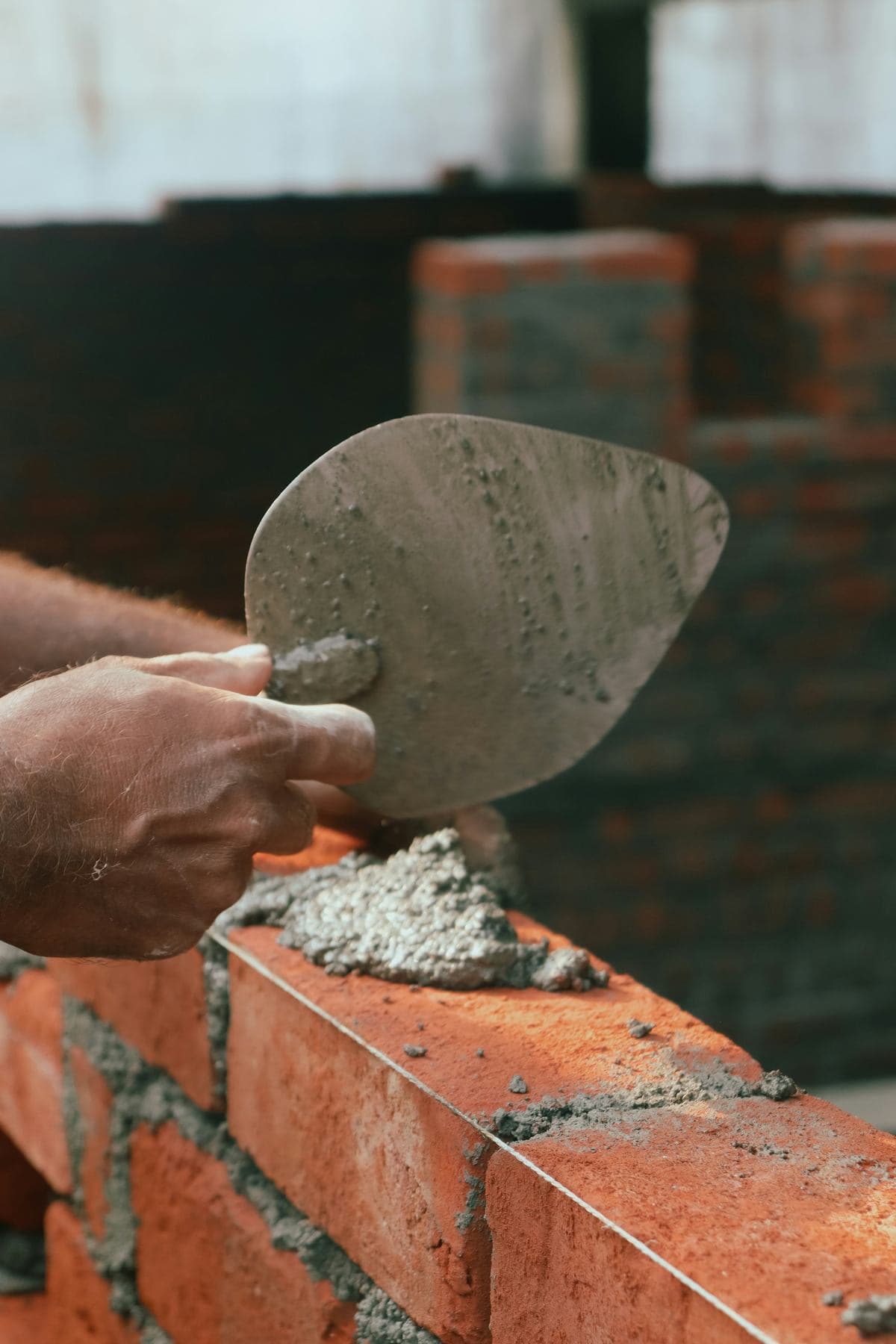 A bricklayer's trowel laying mortar on a course of red brick