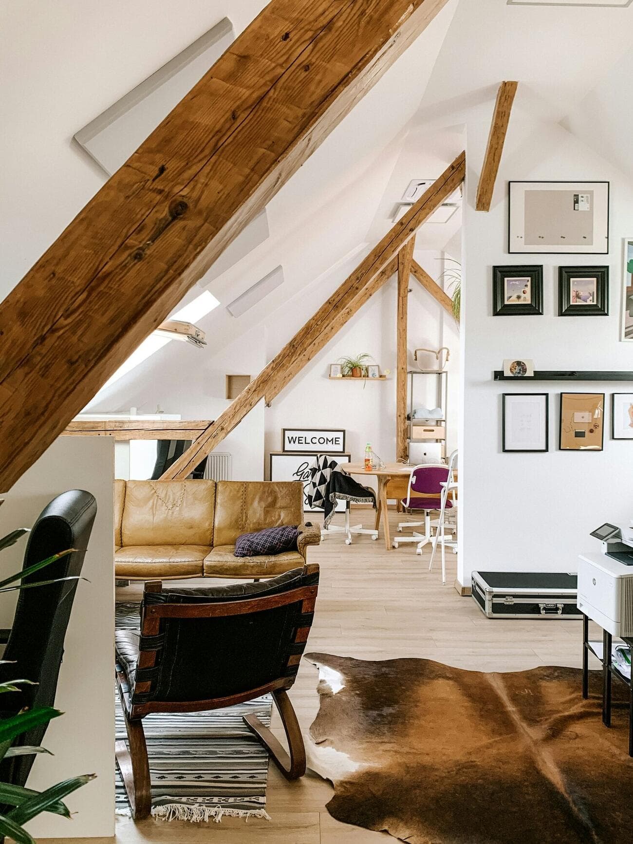 A loft room under exposed oak rafters, with a leather chair, rugs and daylight from roof windows