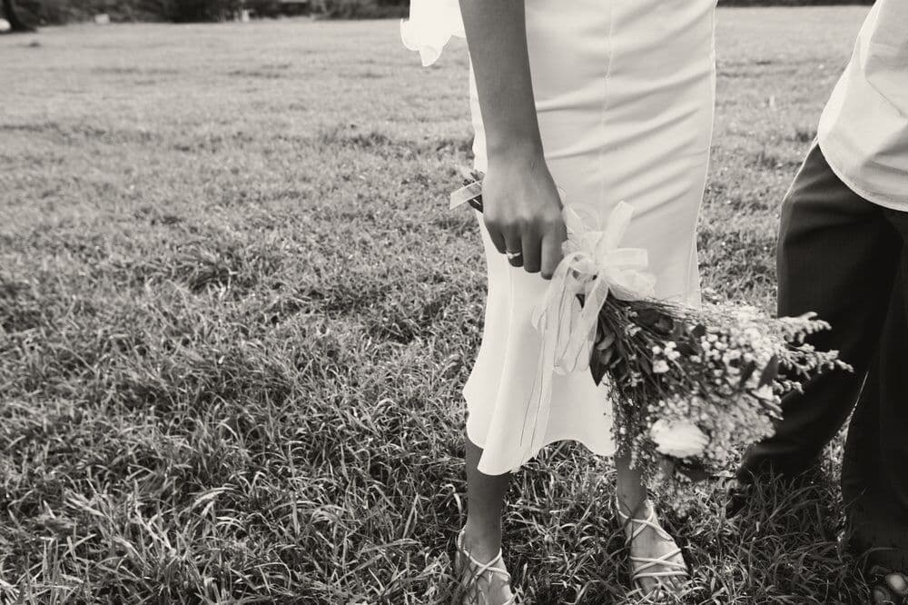 A bride holds her bouquet low beside her dress on a lawn