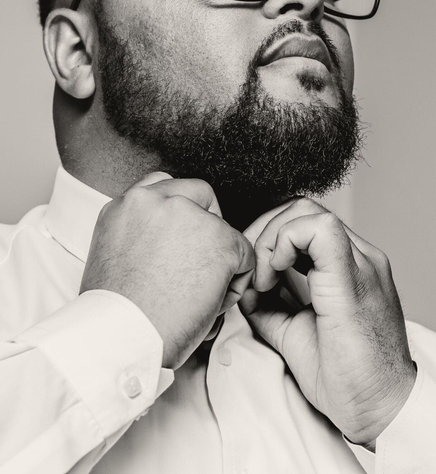 A groom fastens his collar button, head tipped back, in close-up