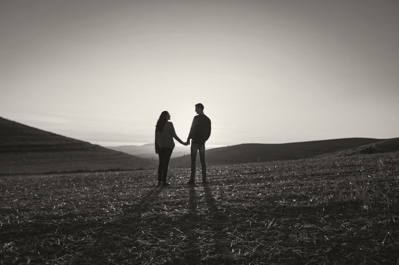 A couple holding hands, silhouetted on a ridge at sunset