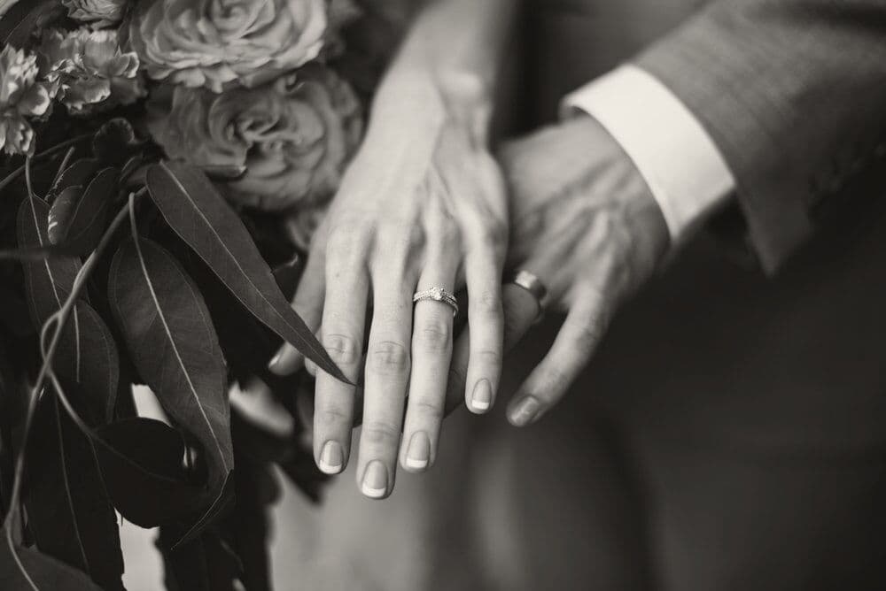 Newly married hands with rings resting beside a bouquet of roses