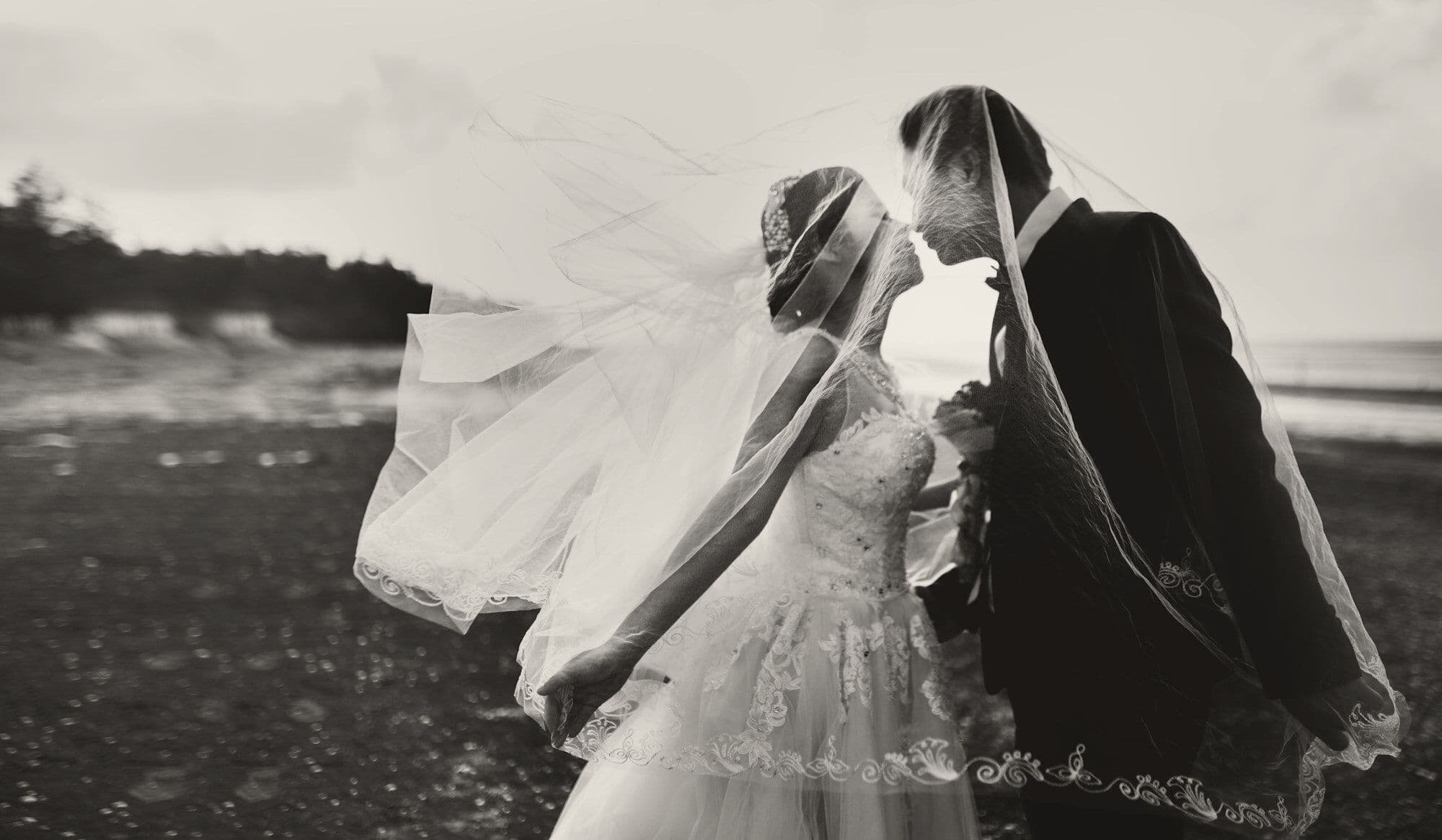 A bride and groom kiss as the wind lifts her veil across an open field