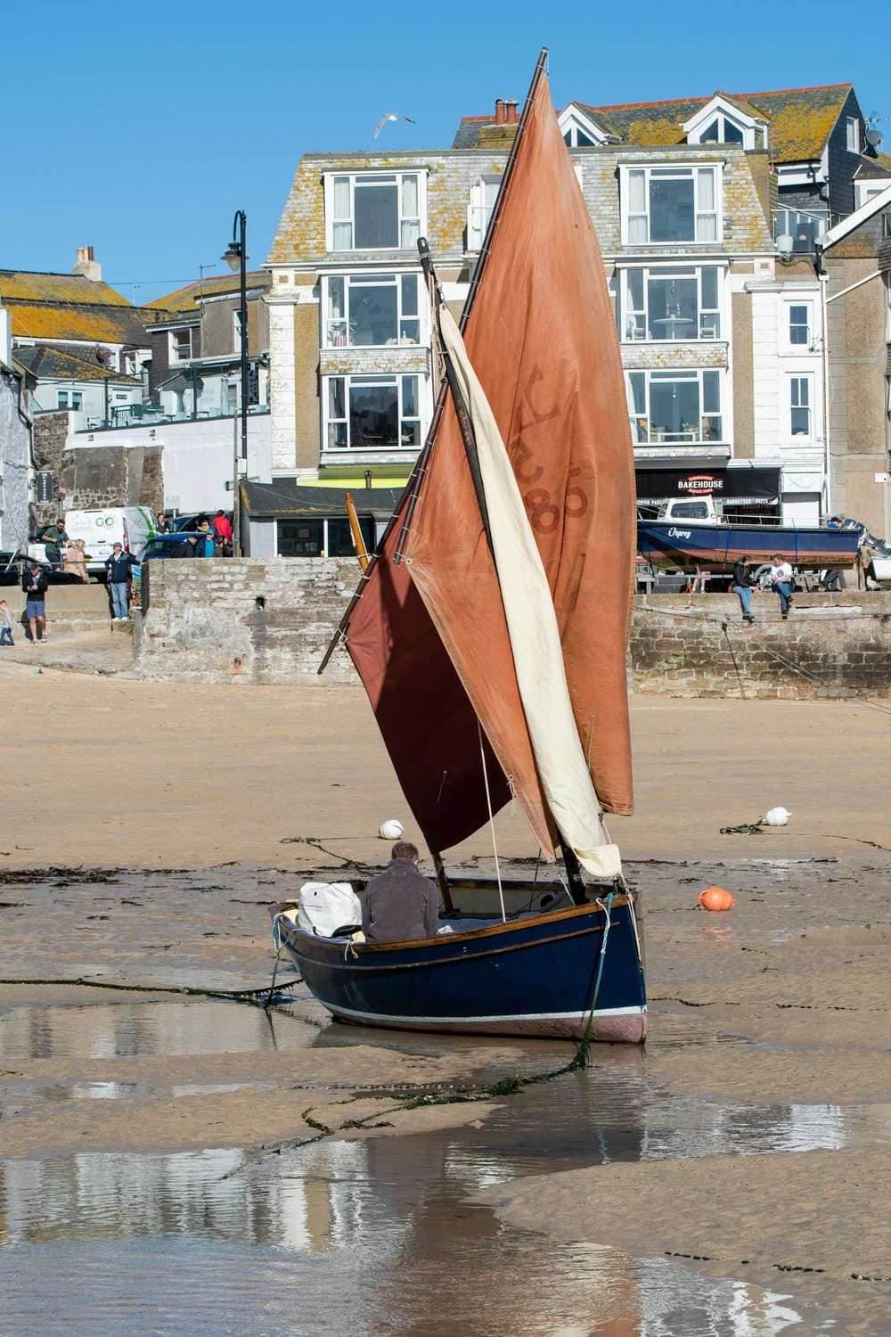 A wooden sailing boat with a red sail resting on the sand at low tide