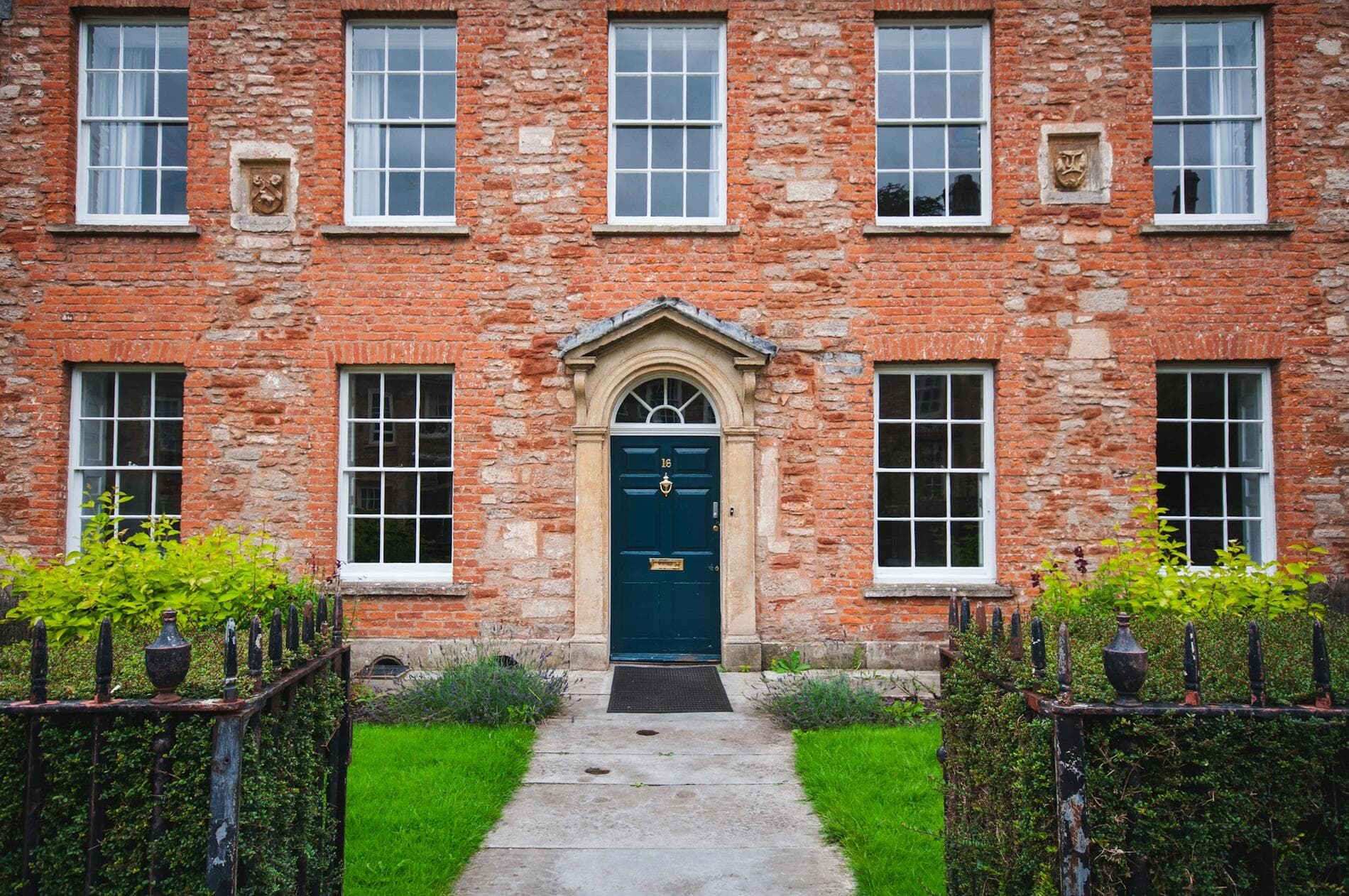 A red-brick Georgian house with white sash windows, a dark green front door and a stone path between clipped hedges