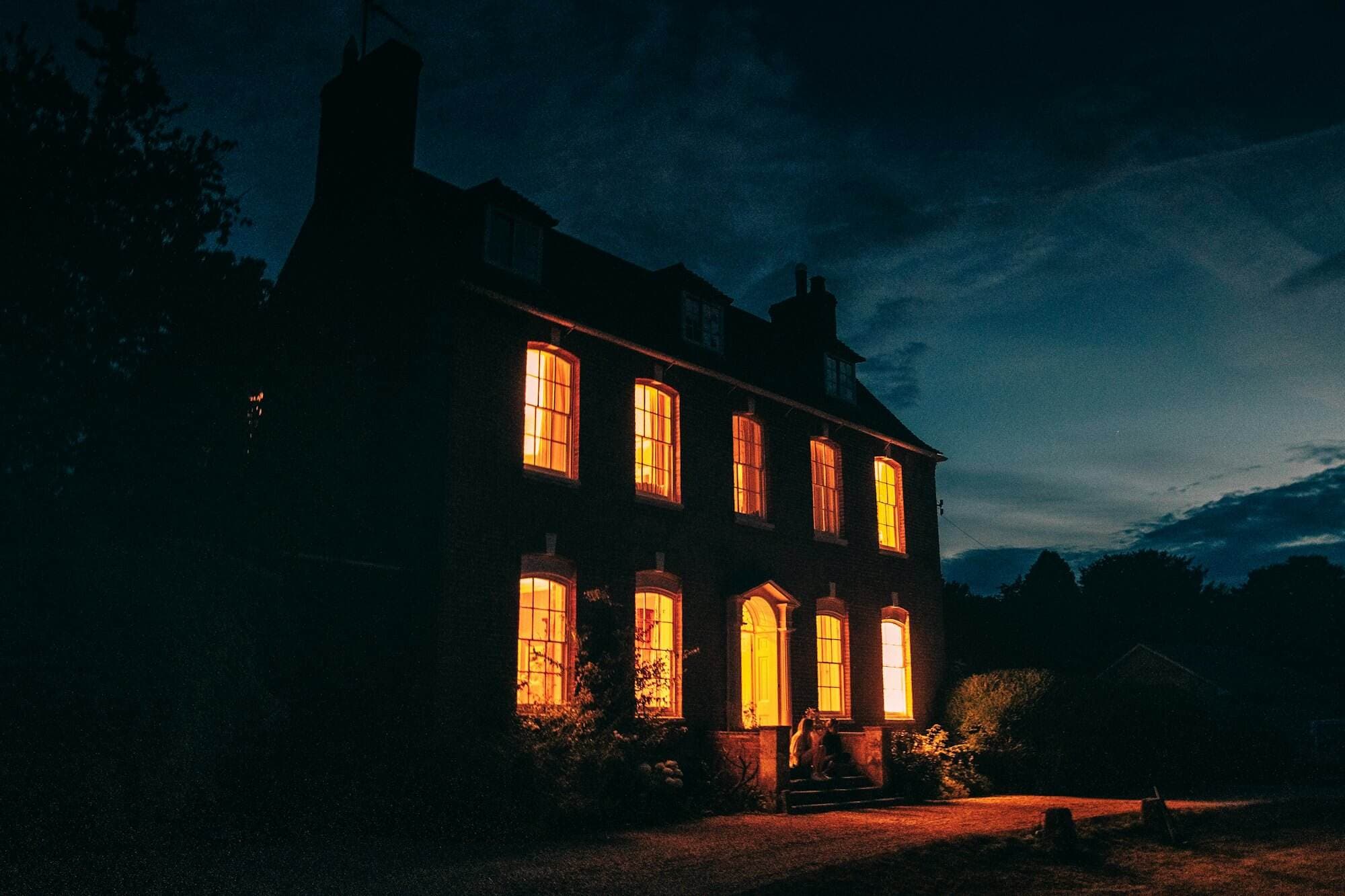 A tall Georgian house at dusk with every window lit warm gold against a deep blue sky