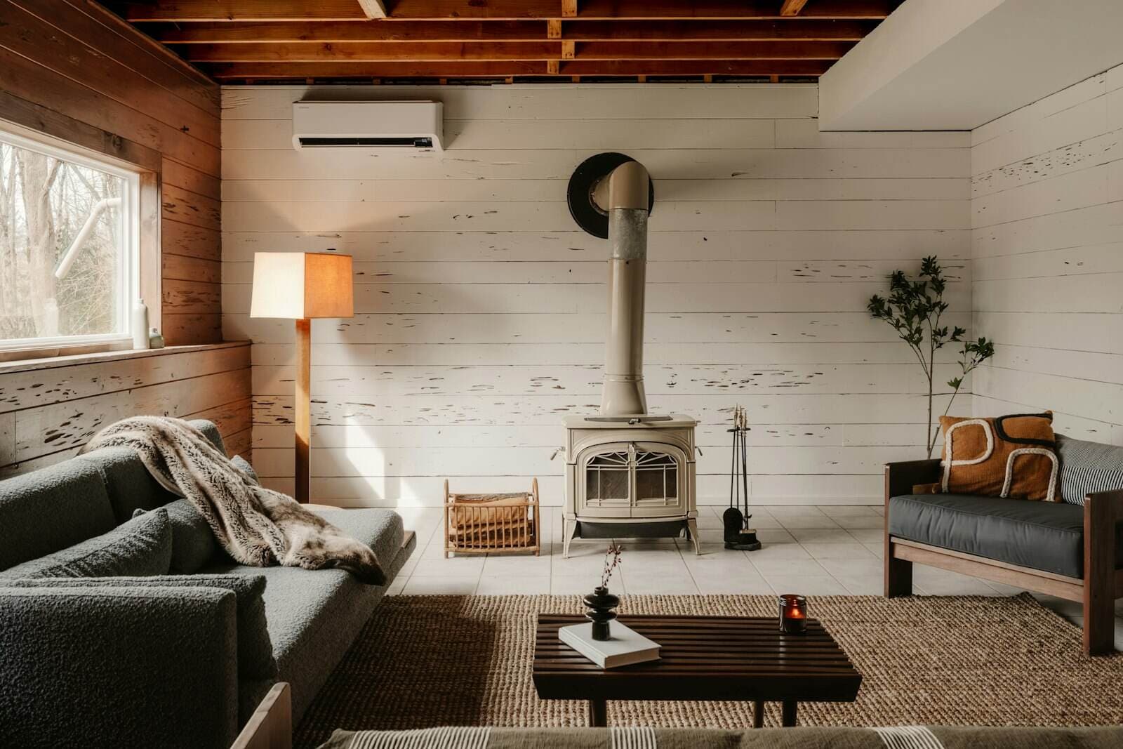 A bright cottage sitting room with a wood-burning stove, a deep sofa and a timber ceiling
