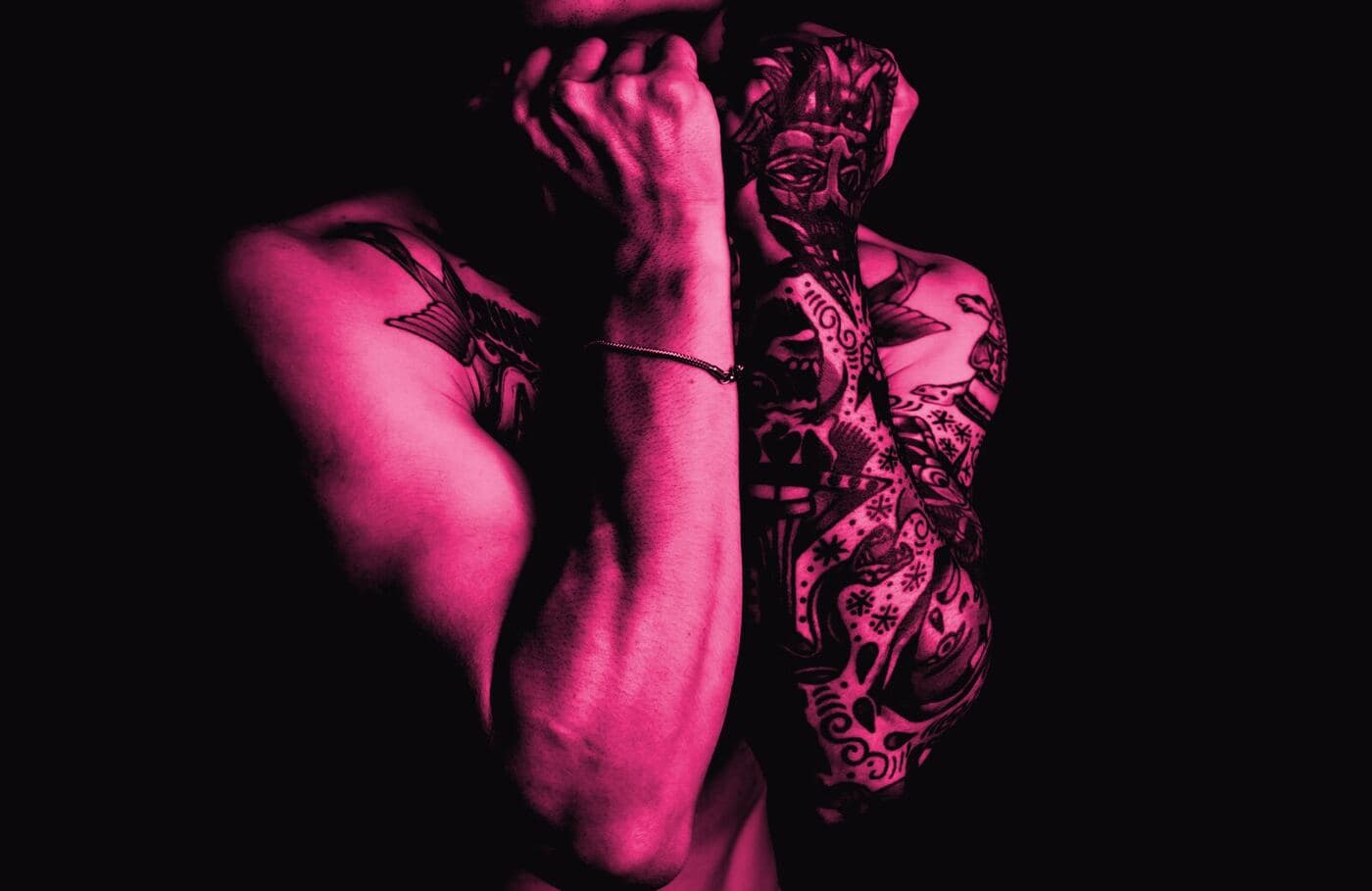 A heavily tattooed arm and torso lit from the side