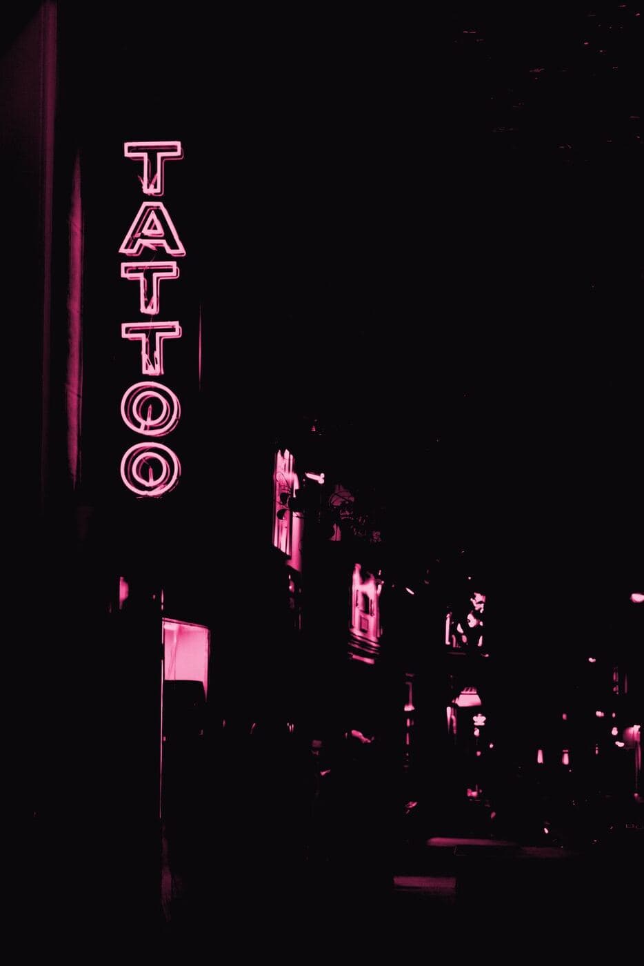 A vertical neon TATTOO sign glowing over a dark street at night