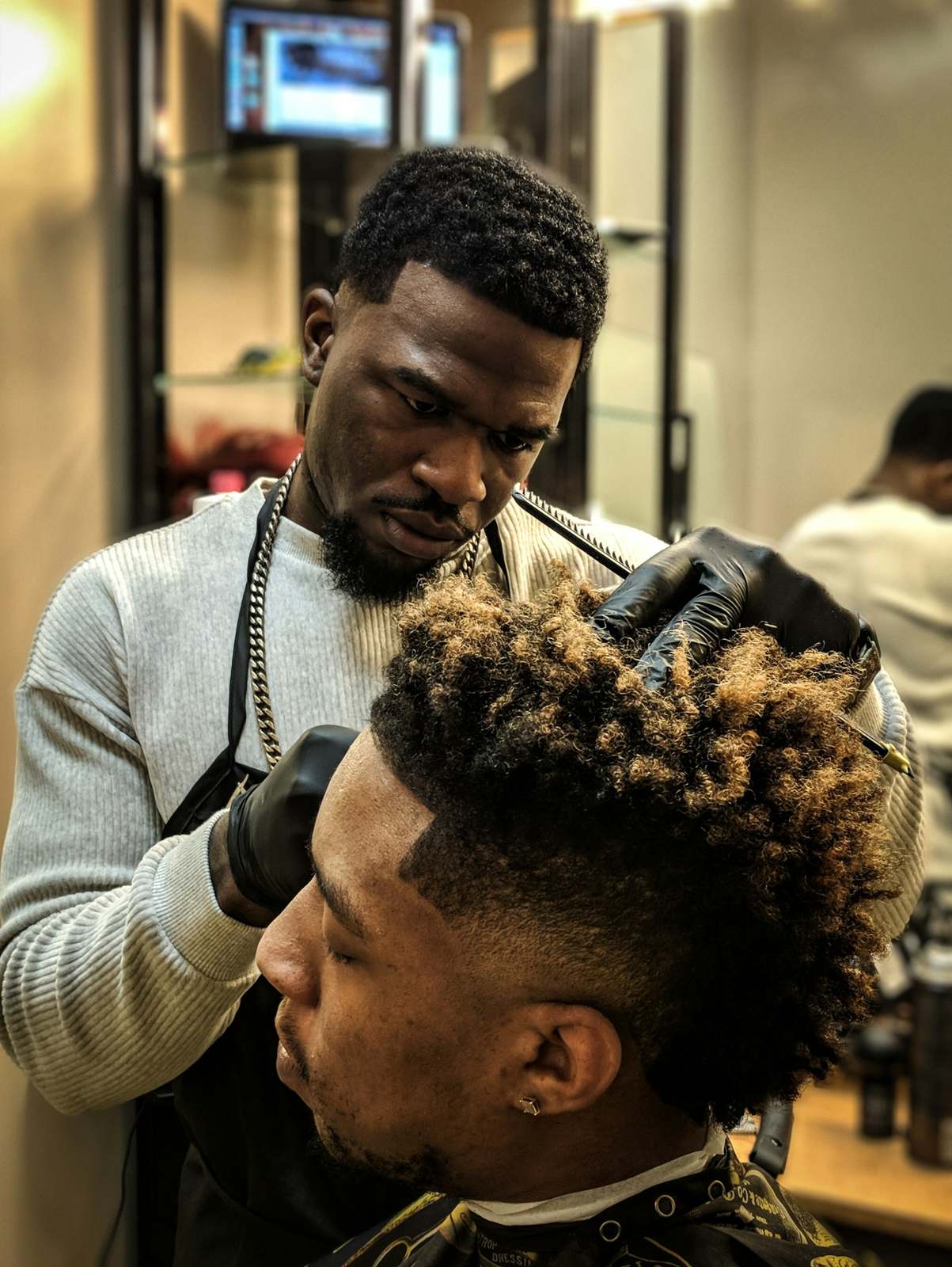 A barber in black gloves shaping a textured curly top with clippers