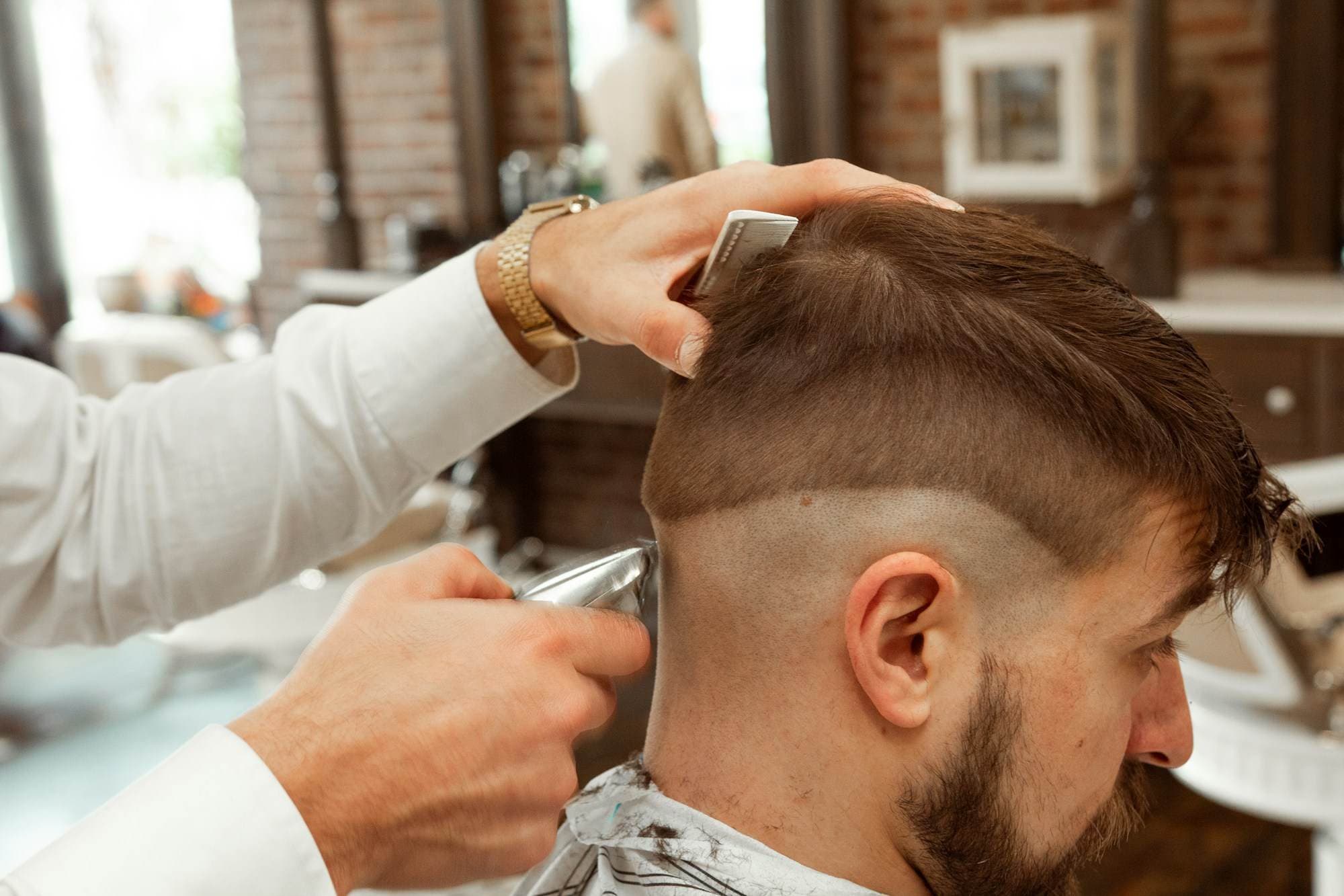 A barber taking a skin fade down with clippers, the customer in a striped gown