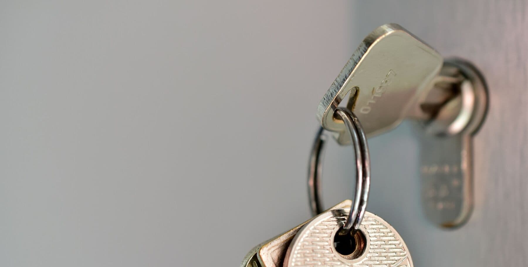 A key on a ring turned in a euro cylinder lock on a pale grey door