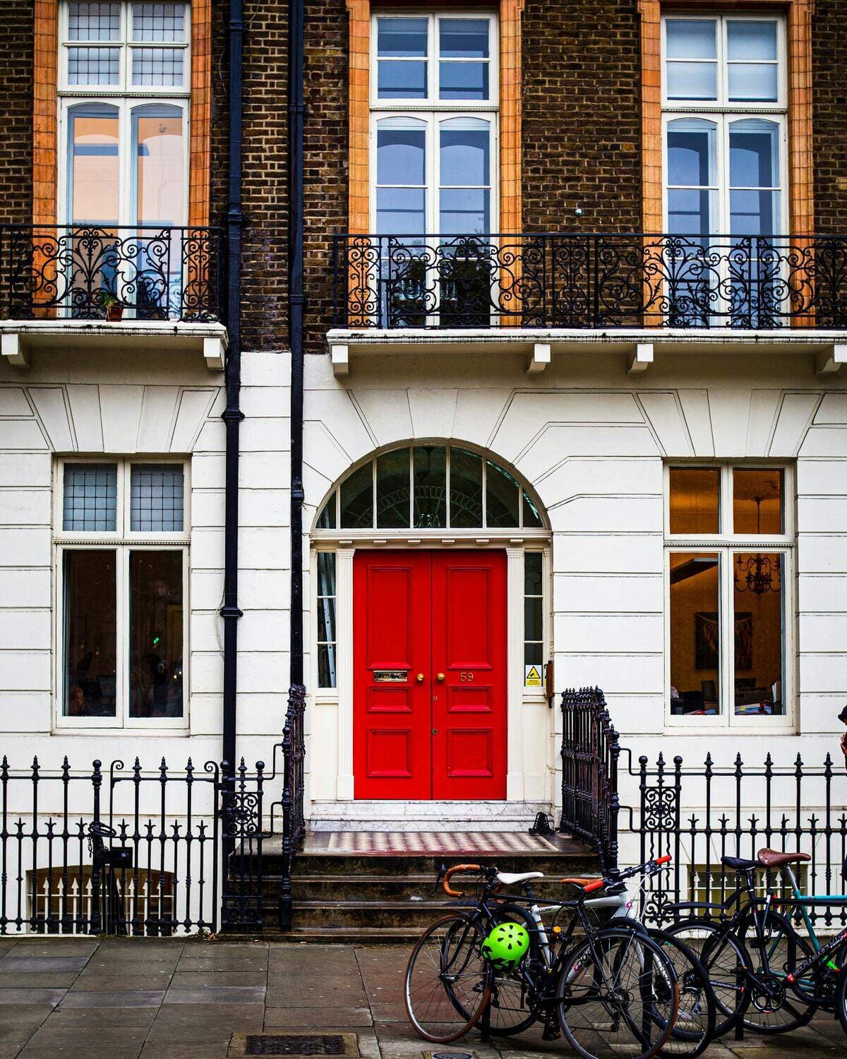 A red front door under an arched fanlight in a white Georgian terrace, with railings and bicycles outside