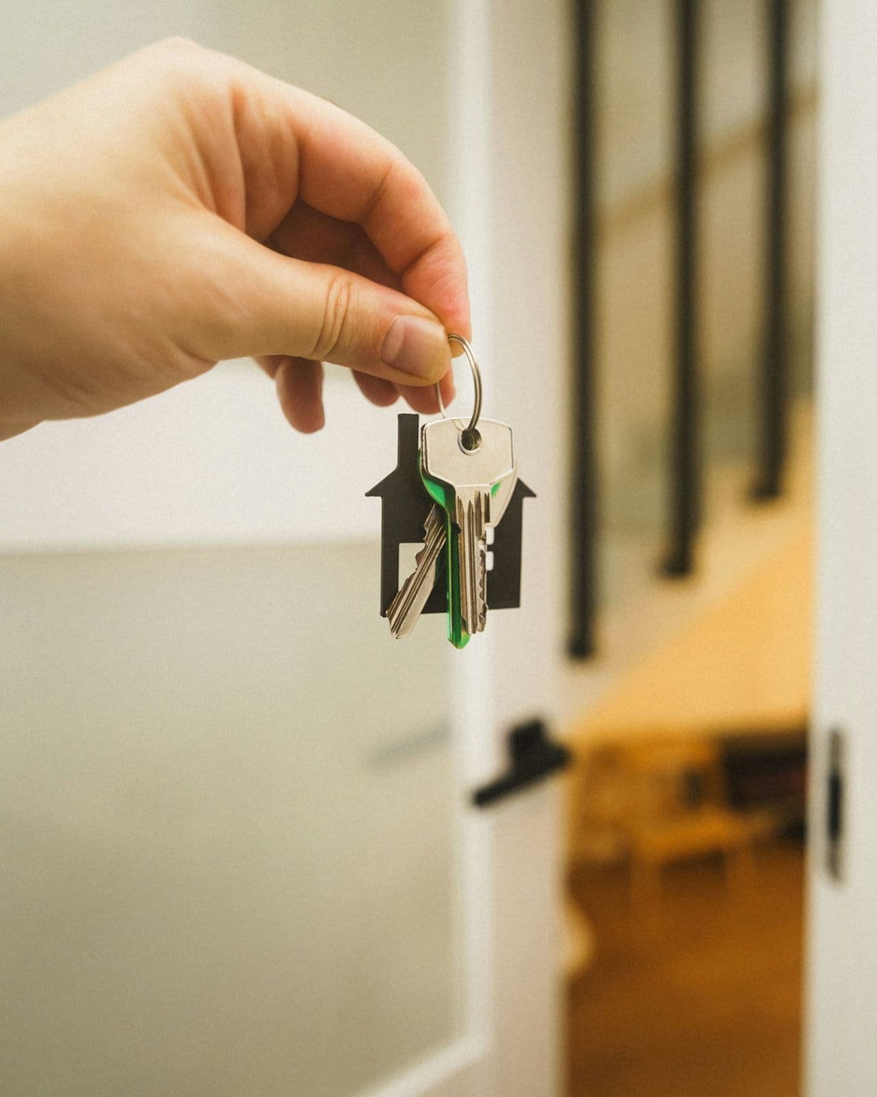 A hand holding up a set of house keys in front of an open white door