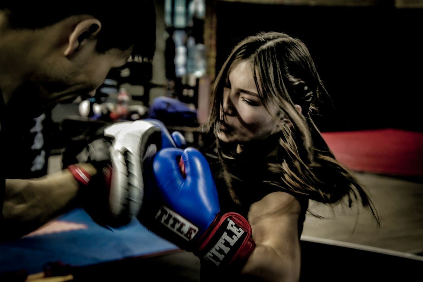 A woman throwing a punch on the pads, held by her coach in a boxing gym