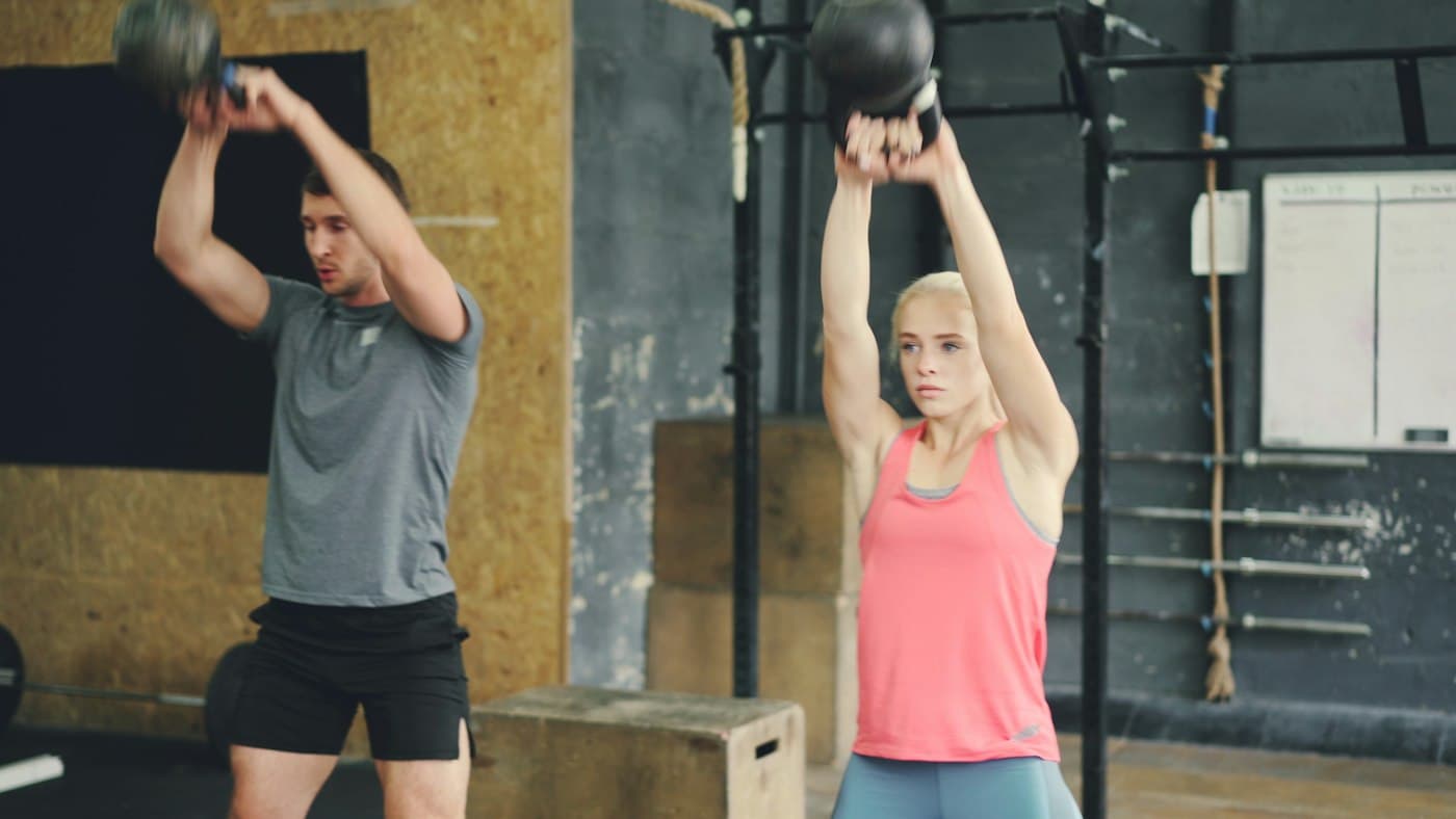 A man and a woman swinging kettlebells side by side in the studio