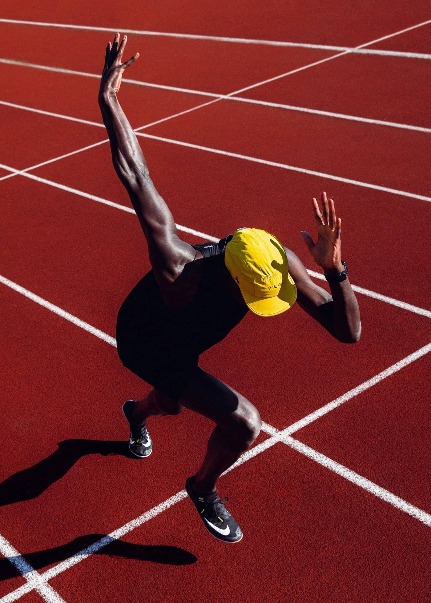 An overhead view of a runner in a yellow cap bursting off the start line on a red track