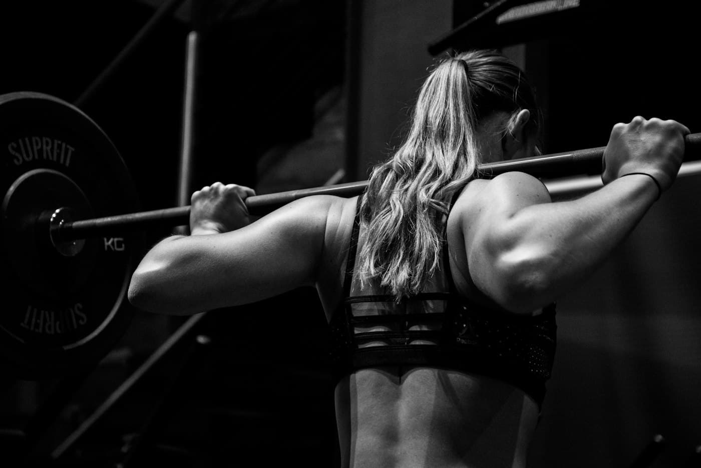 A woman in a dark gym holding a barbell across her back before a squat
