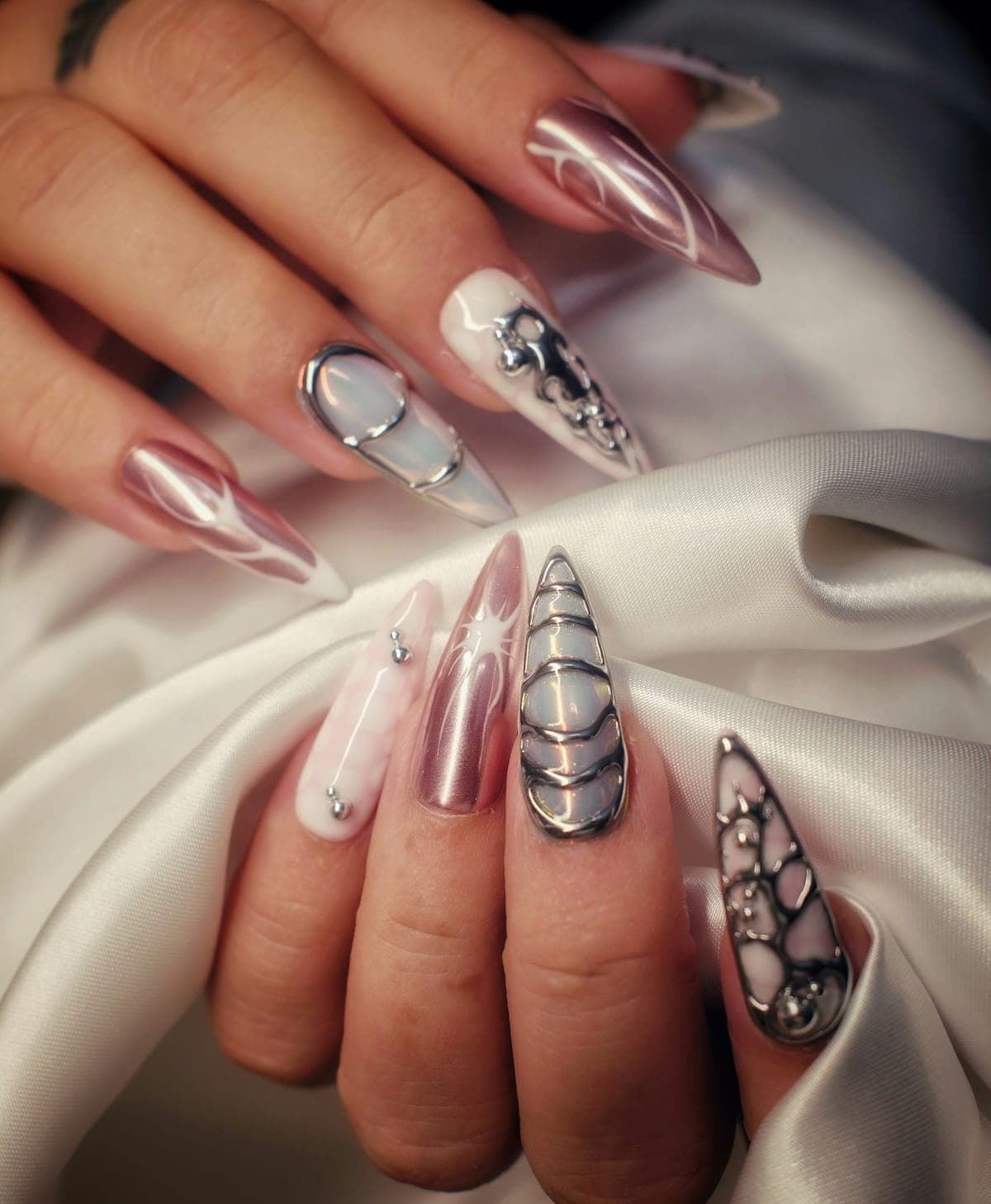 Long stiletto nails in pink chrome and white, with raised silver chrome swirls and droplets