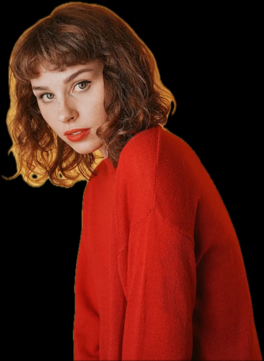 Woman with a wavy copper bob and fringe, in a red jumper, glancing over her shoulder