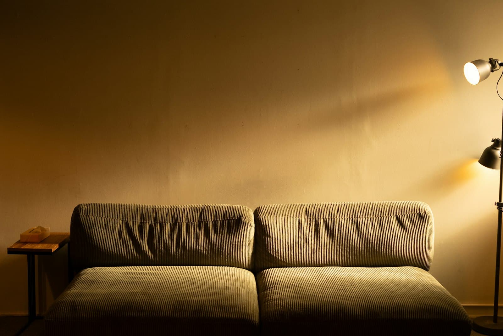 A deep olive sofa against an ochre wall, lit by a single black floor lamp