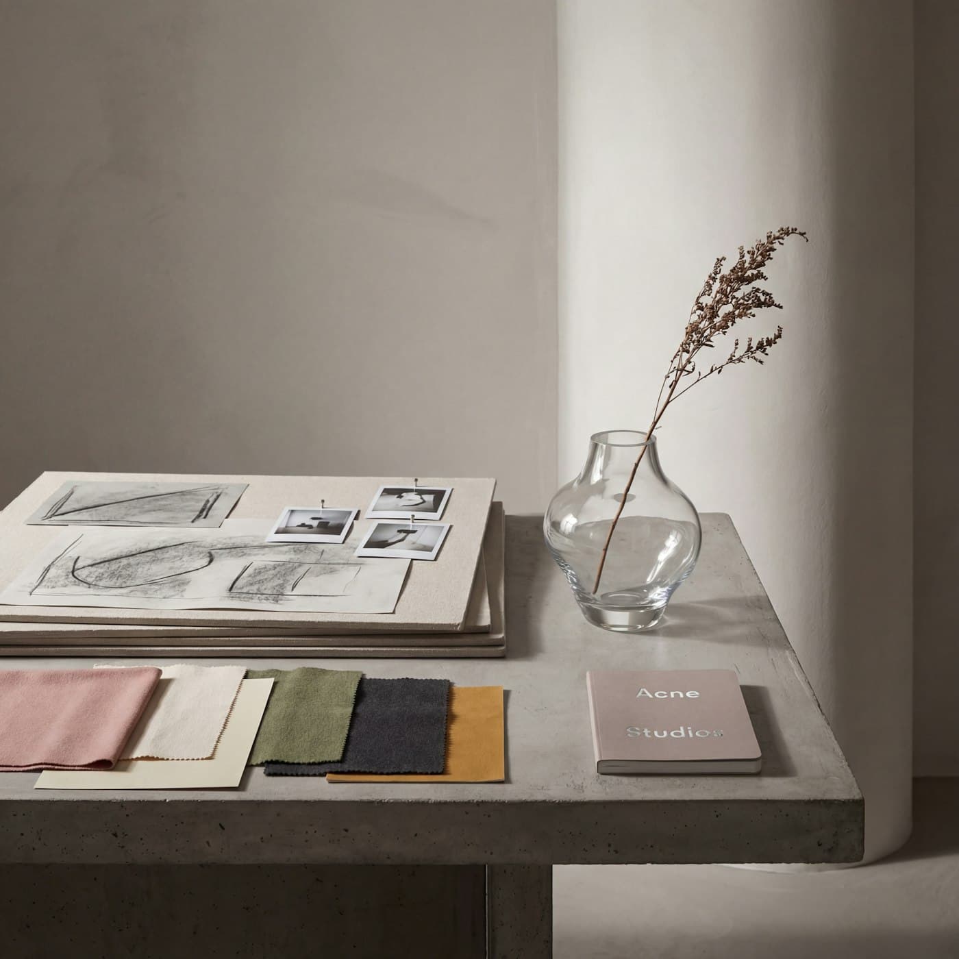 Fabric swatches, sketches and a glass vase with a dried stem on a plaster console