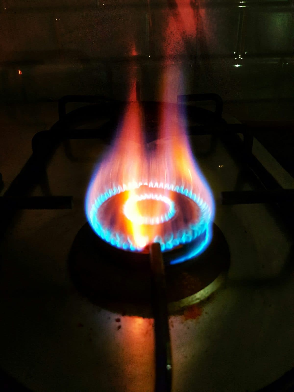A blue gas flame burning on a hob burner in the dark