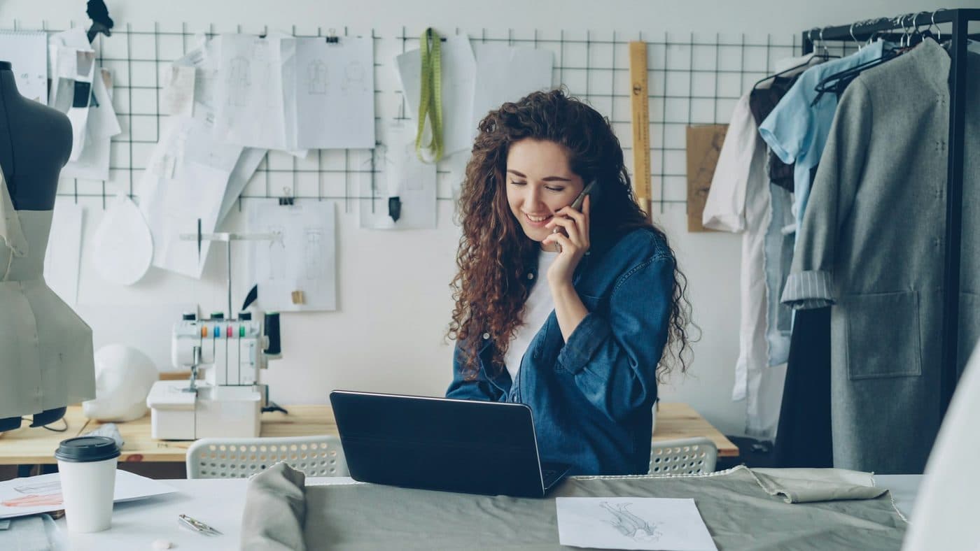 A self-employed designer on the phone at her laptop in a bright studio