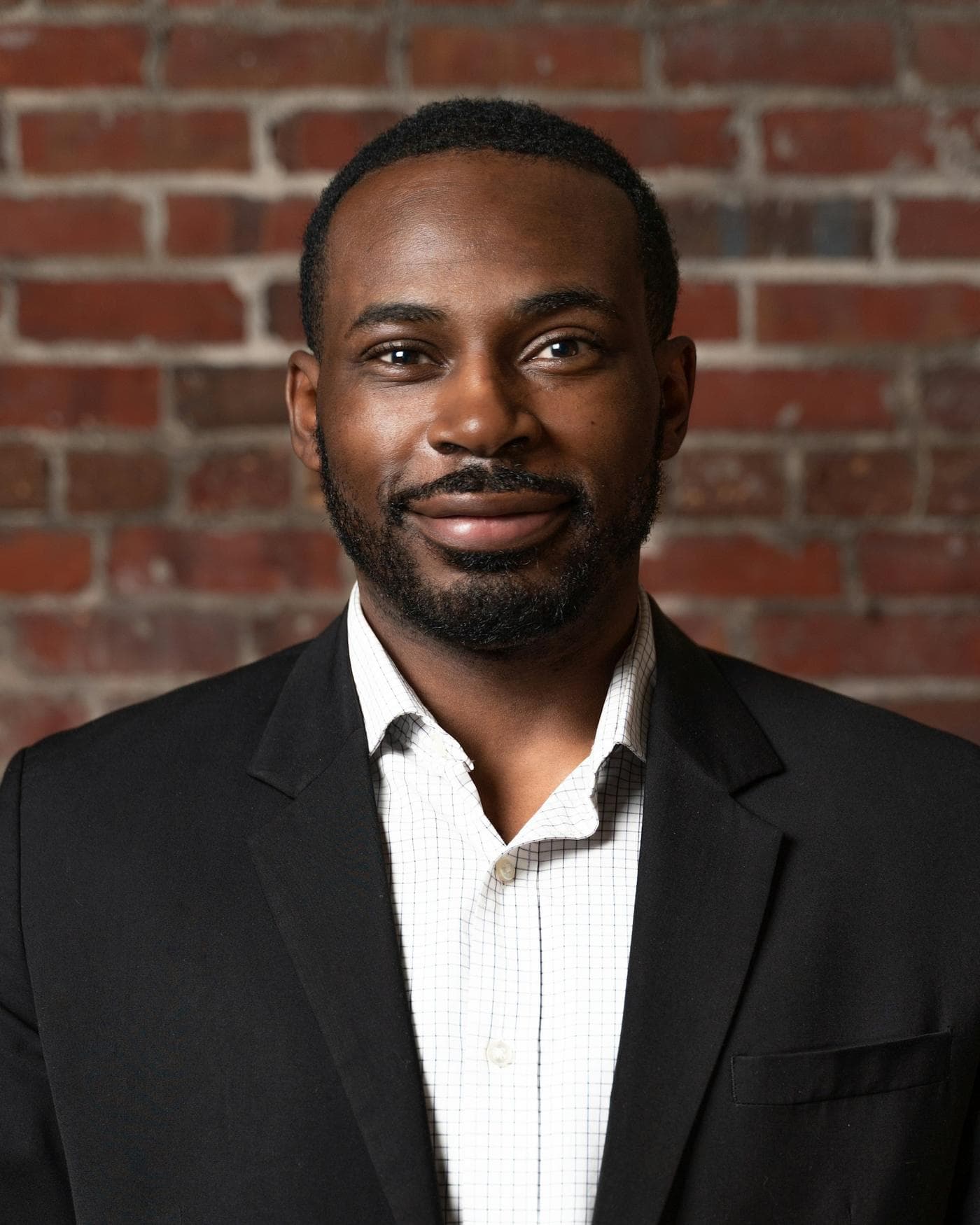 Portrait of Samuel Adeyemi in a dark suit against a brick wall