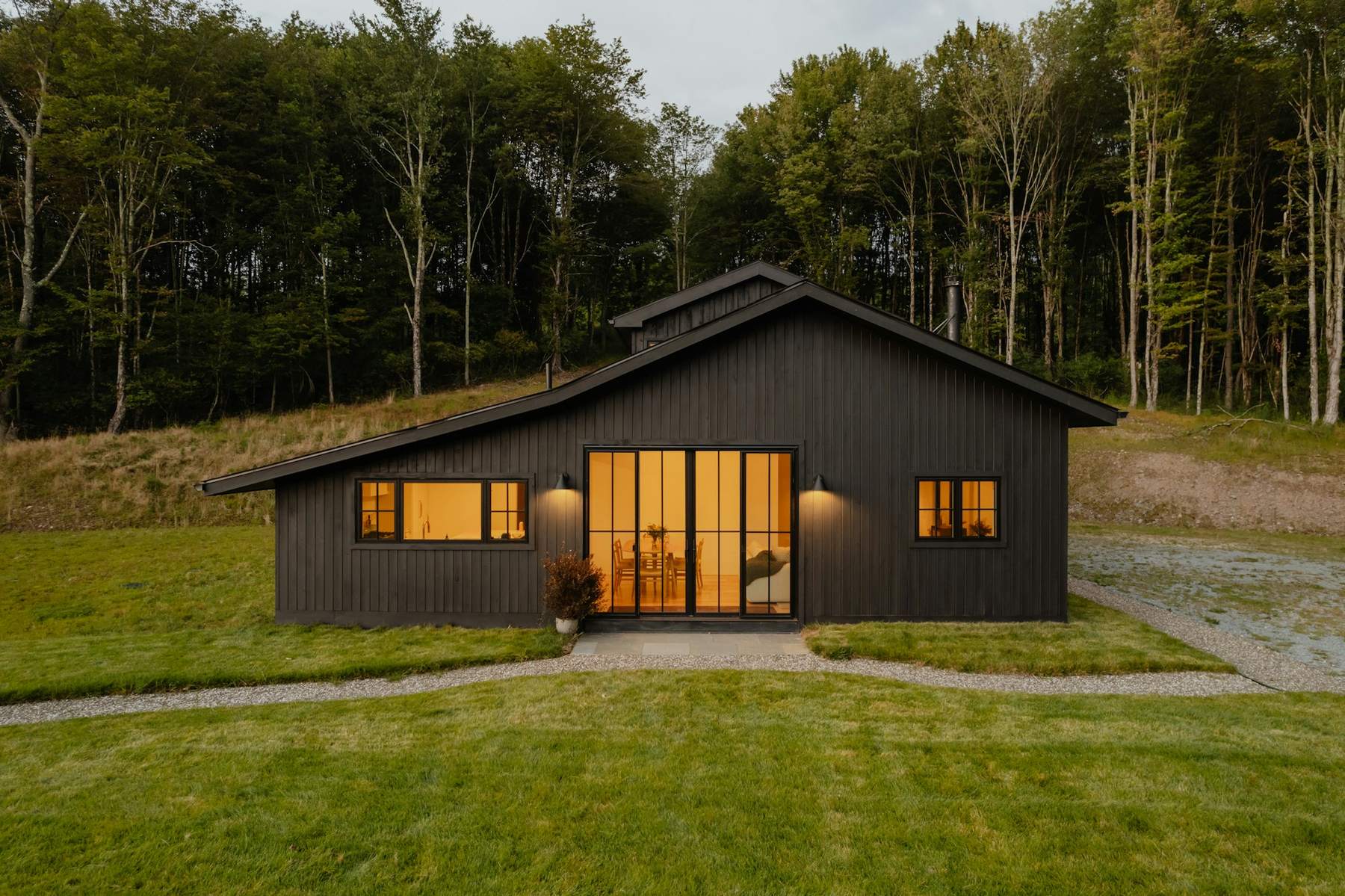 The finished Hollow Lane House at dusk: black vertical timber cladding, warm light through tall glazed doors