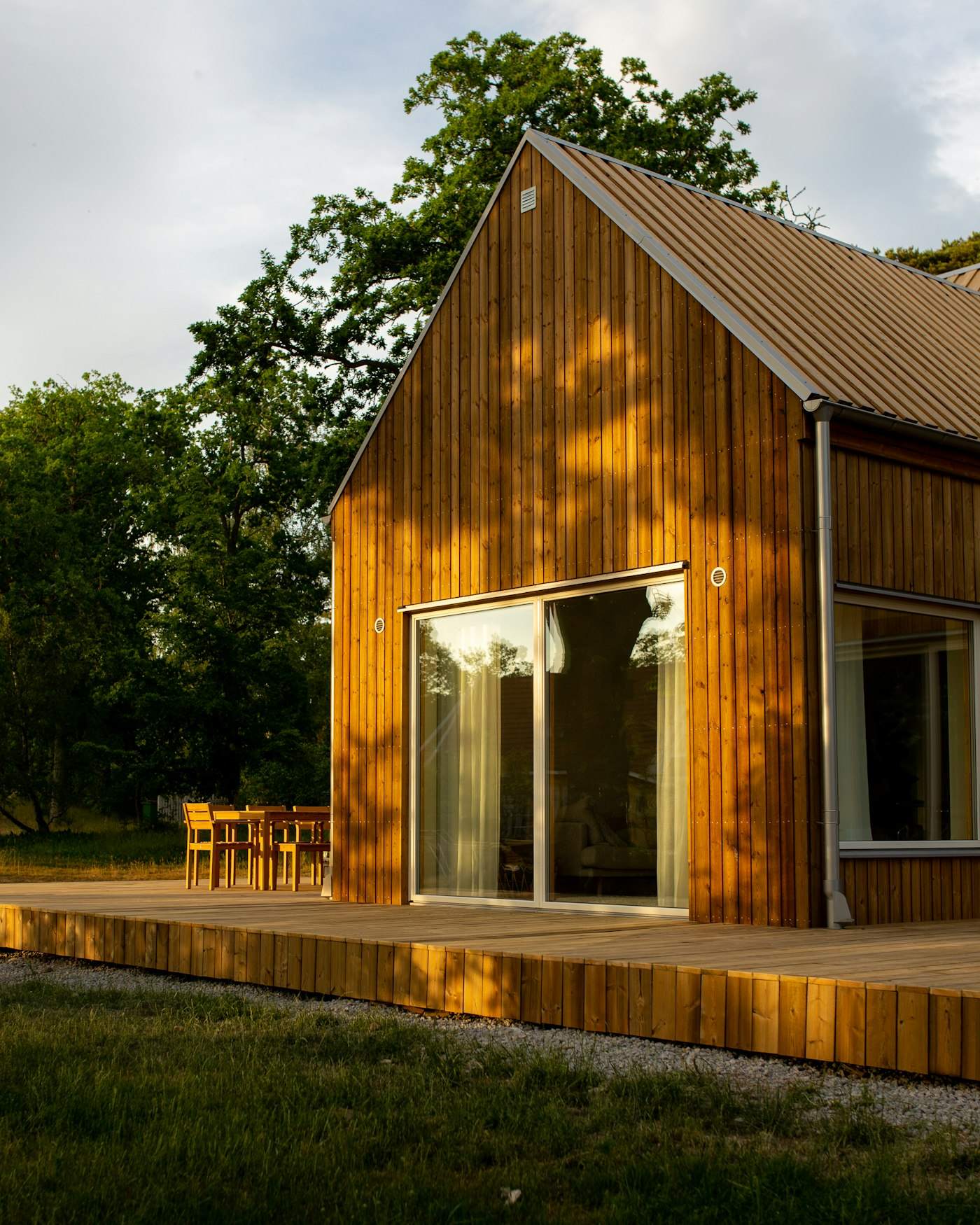 A small larch-clad gabled studio with a big glazed door and a timber deck, among trees