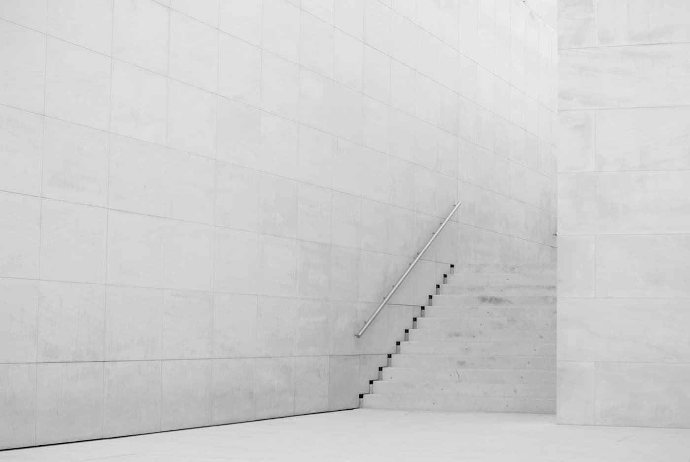 A white concrete stair rising along a plain white wall