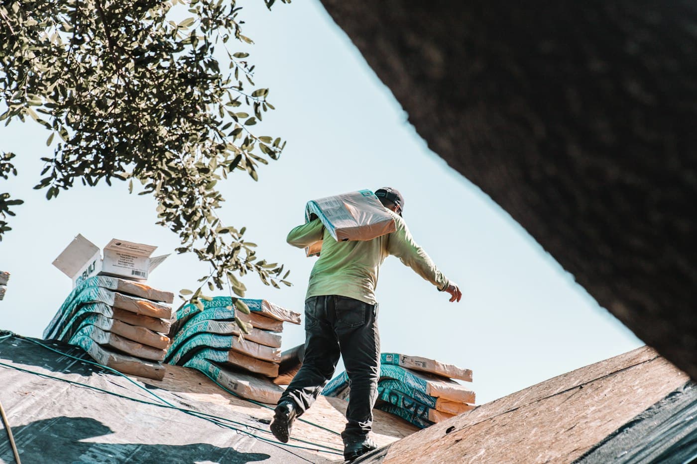 A roofer carrying a bundle of roofing materials across a roof on his shoulder