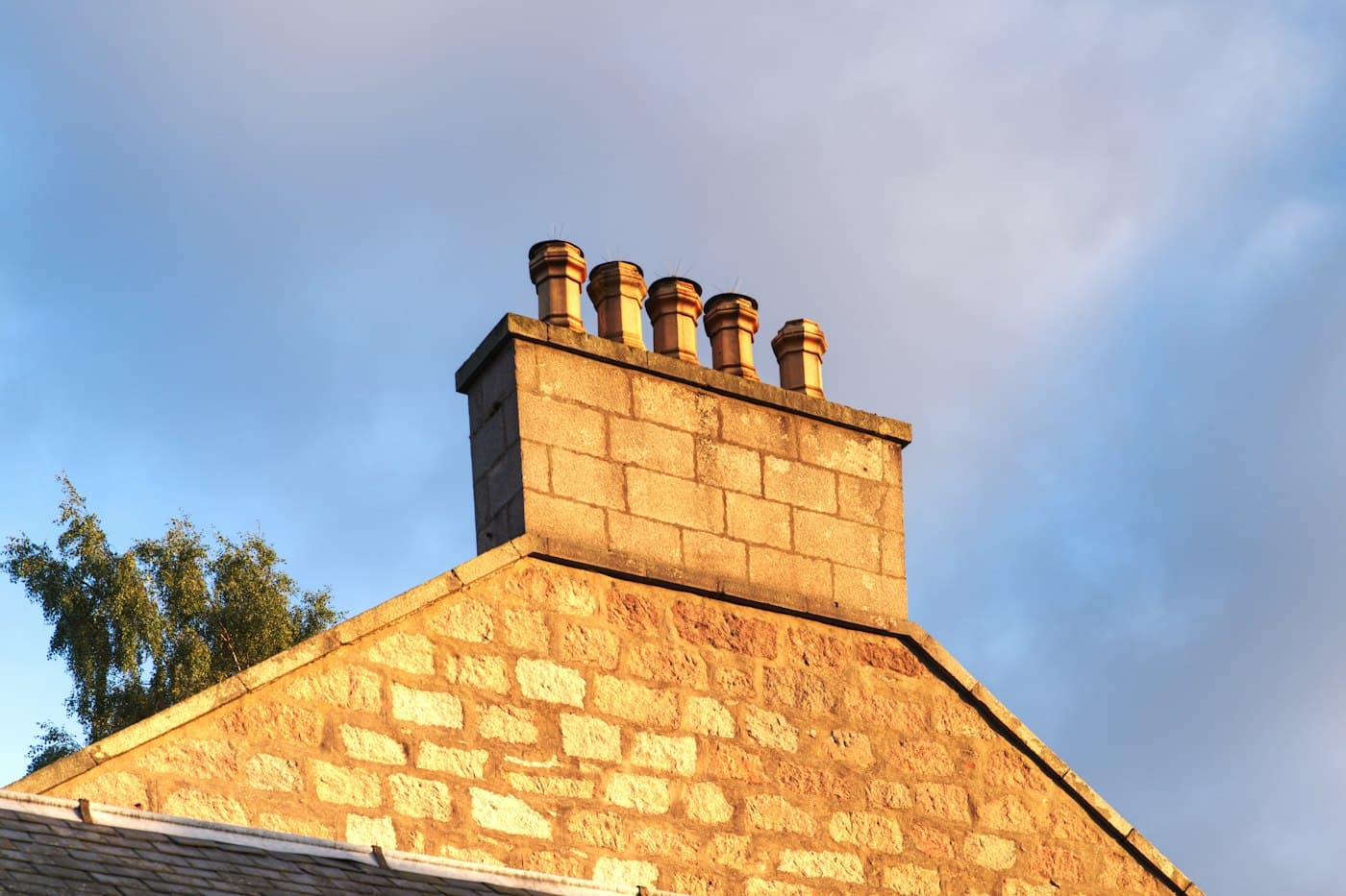 A brick chimney stack with clay pots catching warm evening light