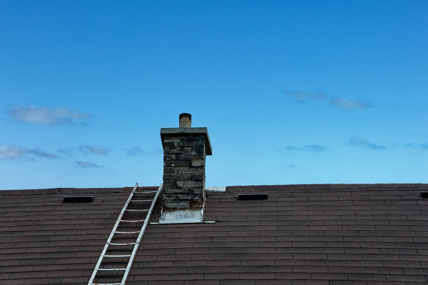 A roof ladder hooked over a ridge beside a chimney, under a blue sky