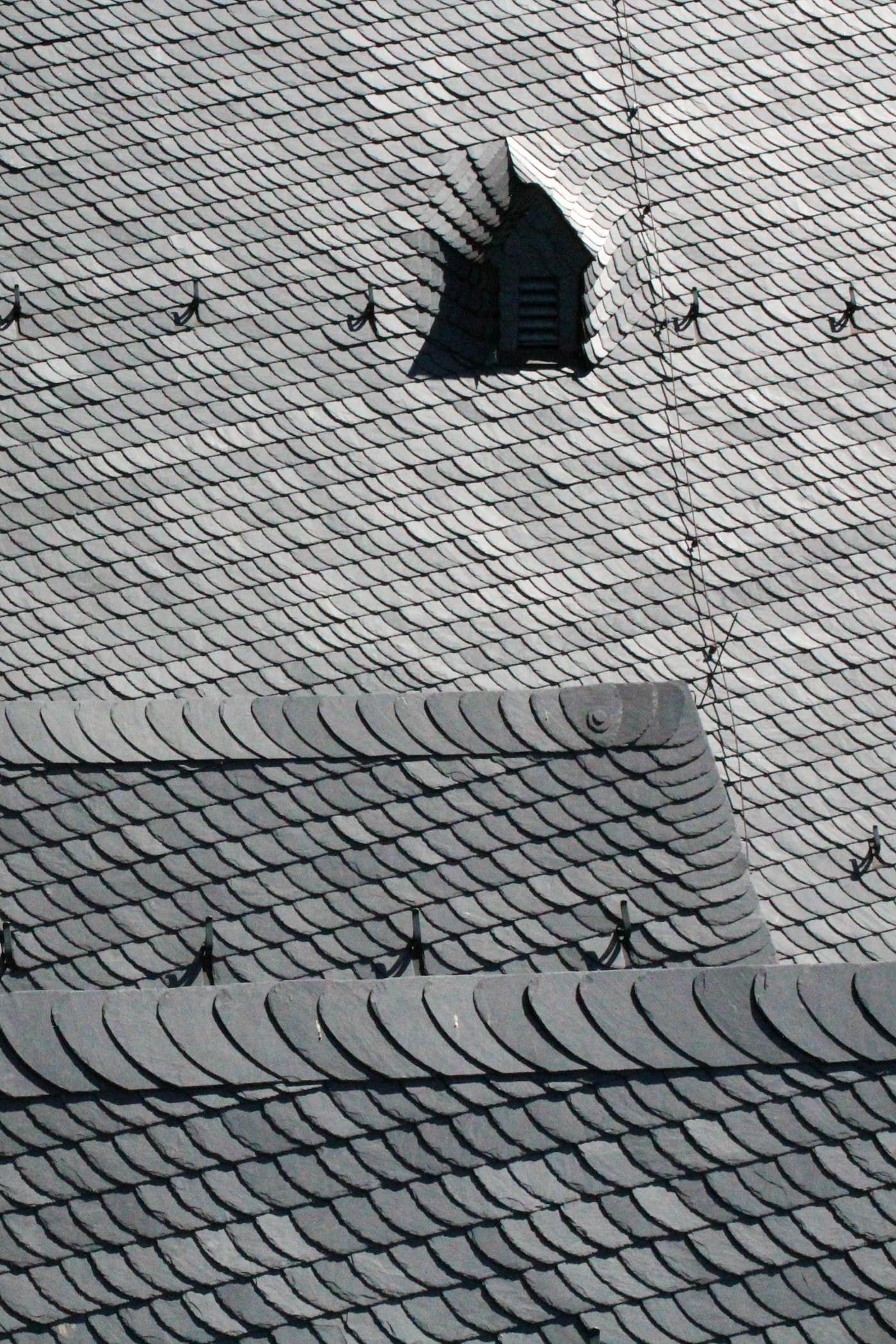 Dark natural slates laid in neat overlapping rows beside a small dormer