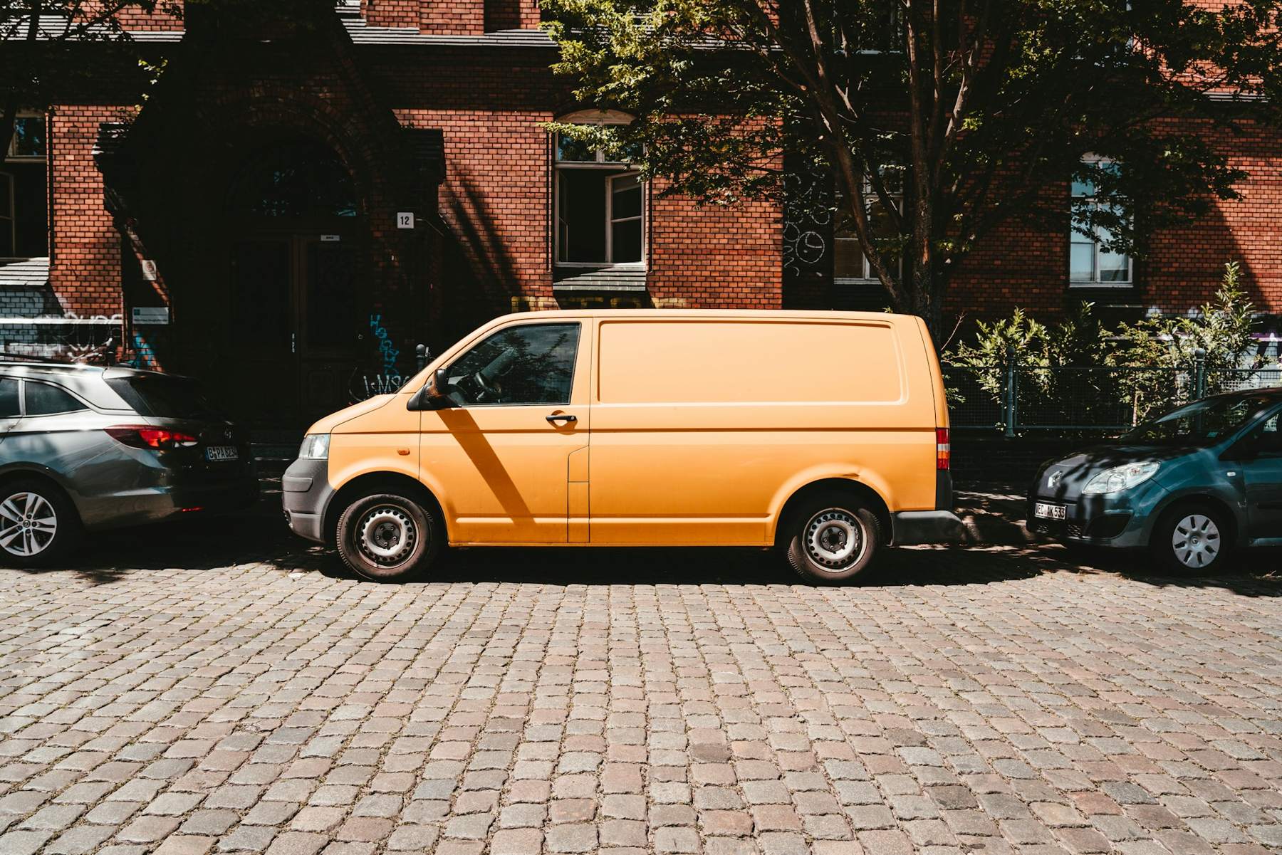 An orange van parked on a cobbled street in front of a red-brick terrace