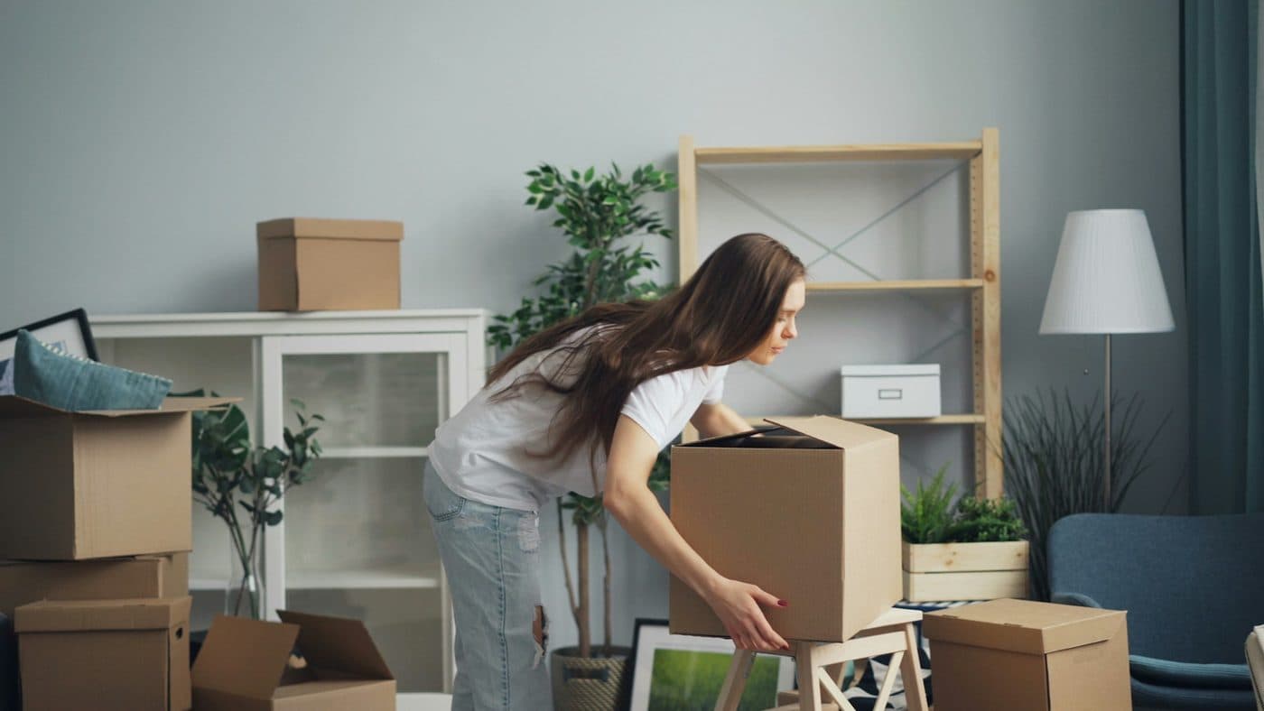 A woman lifting a packed cardboard box in a half-packed living room