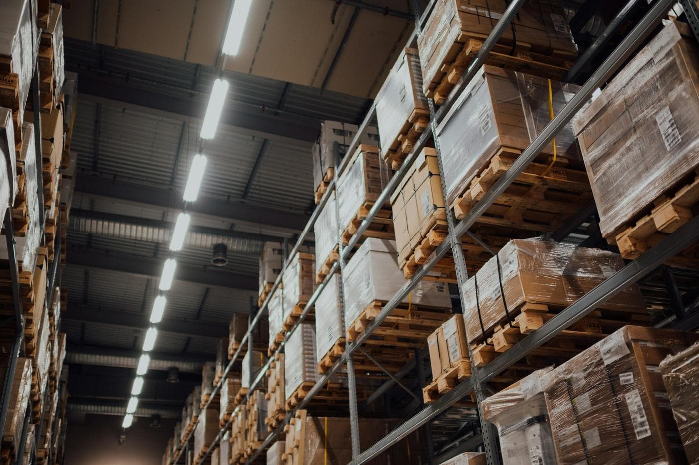 Tall warehouse racking stacked with wrapped pallets and boxes under strip lights
